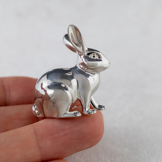 Silver rabbit pendant held in a hand against a plain background
