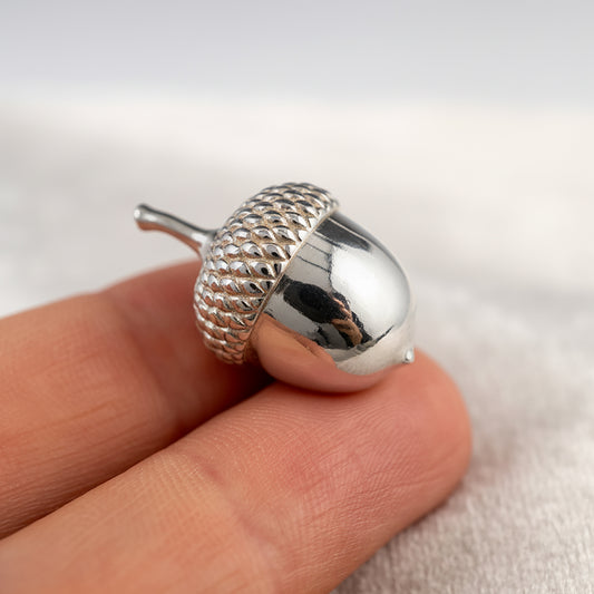 Silver acorn-ornament held between fingers against a neutral background