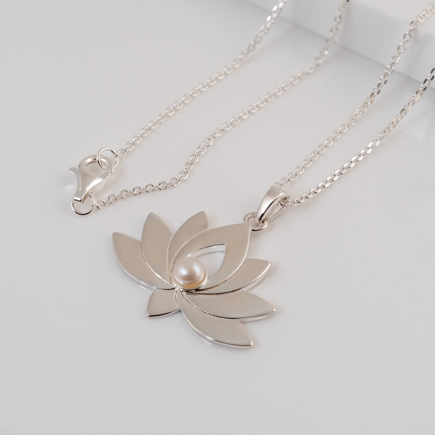 Silver lotus flower necklace with a pearl on a light gray background
