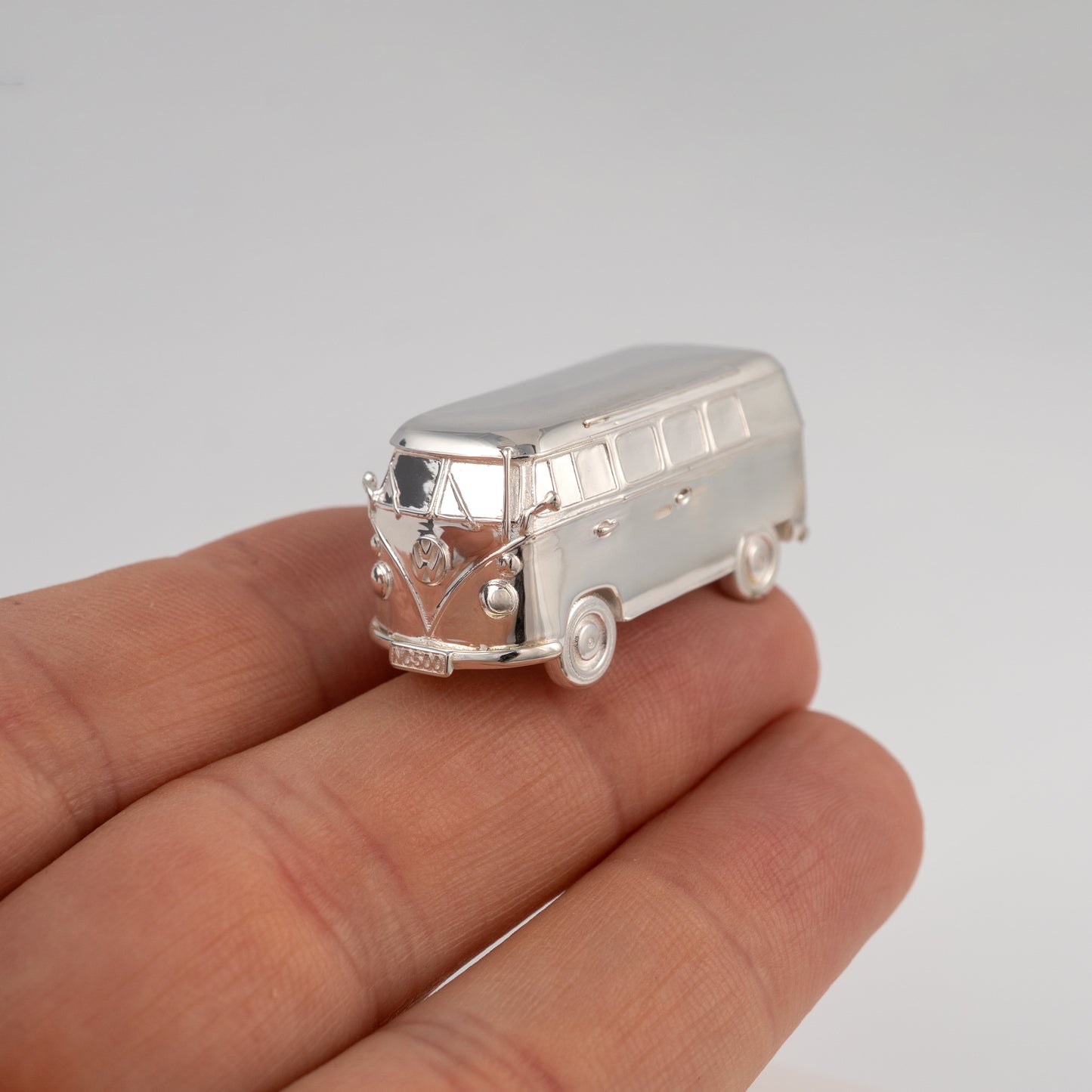 Silver model of a camper van held in a hand against a gray background