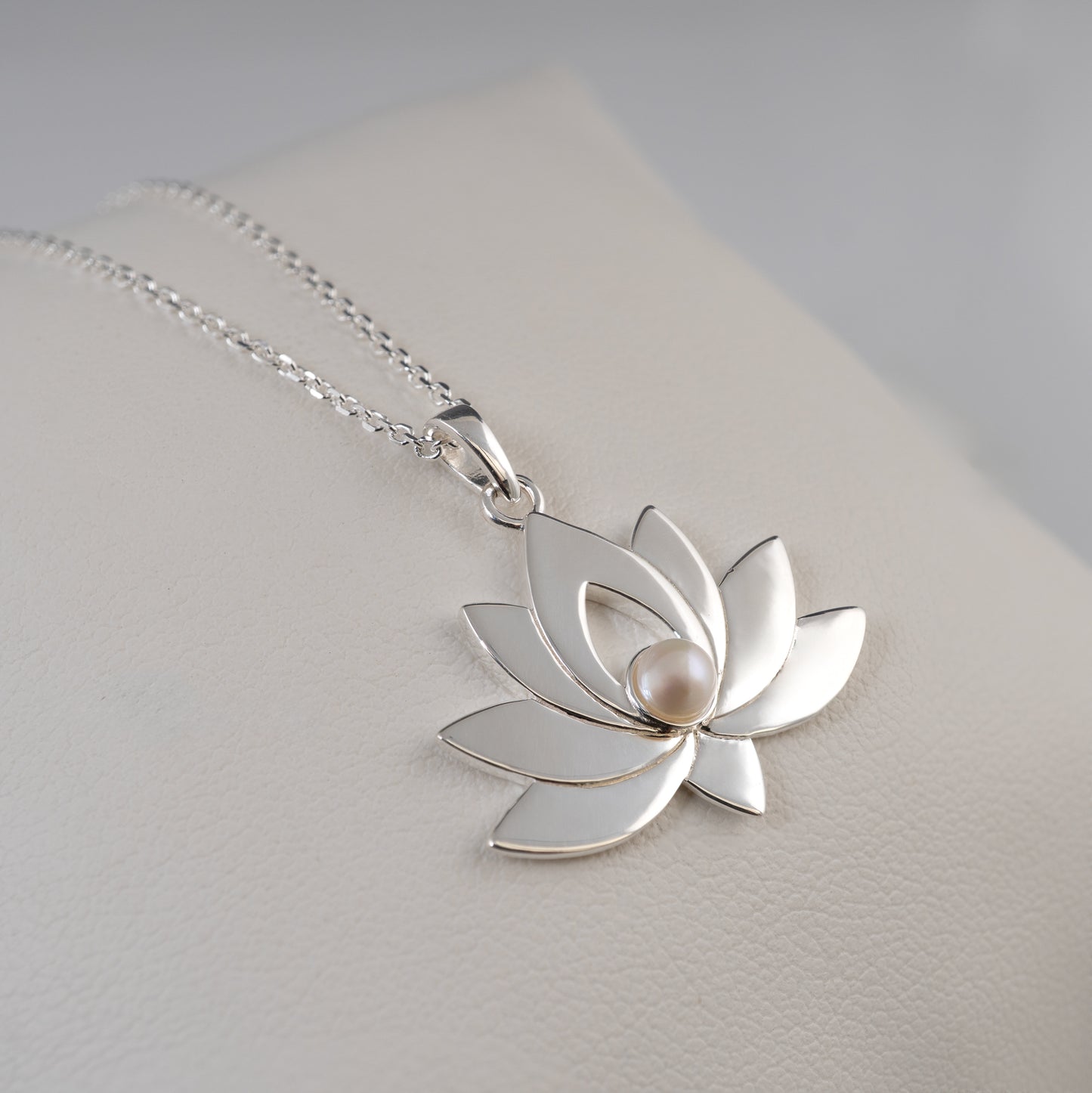 Silver lotus flower pendant with a pearl on a light gray background