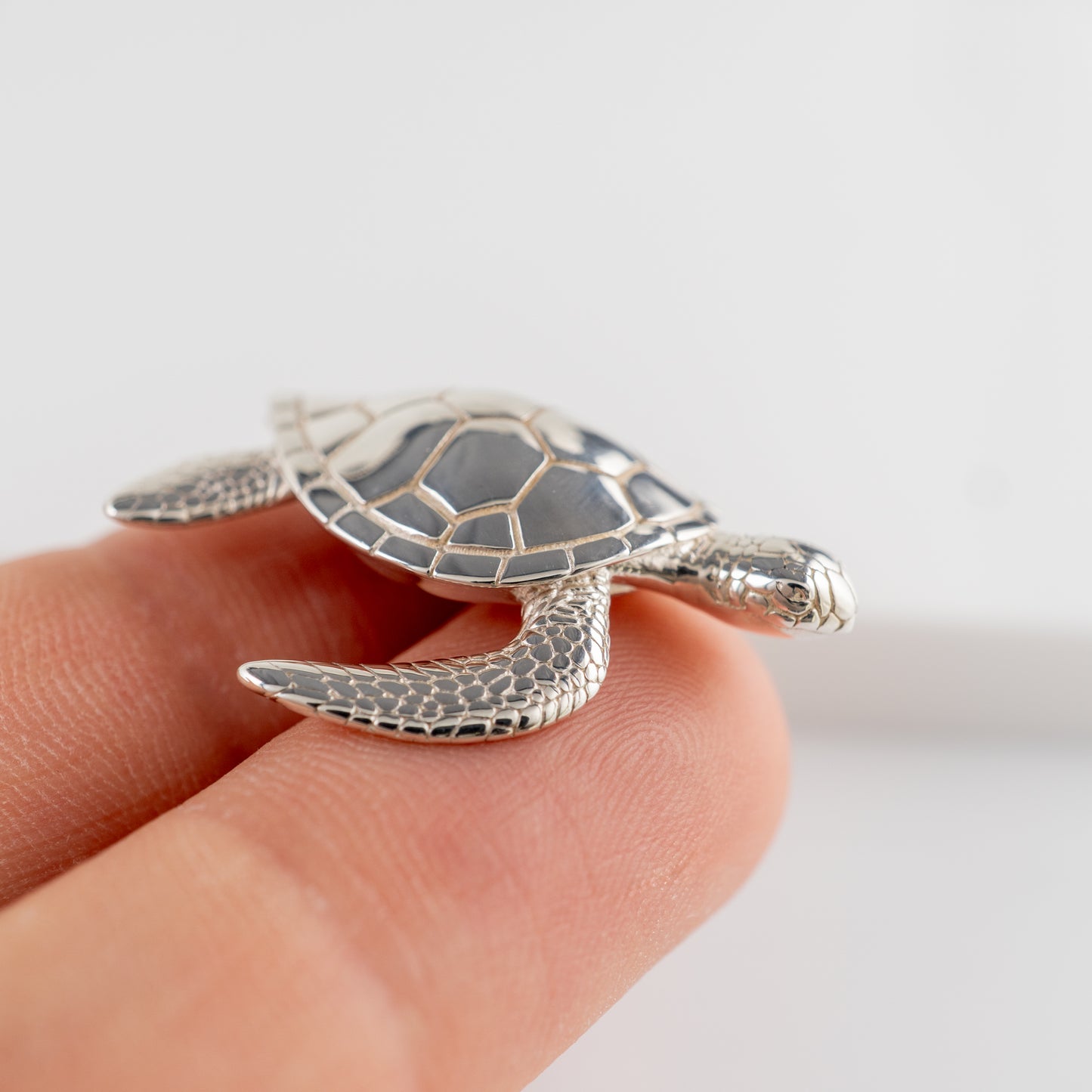 Small sterling silver sea turtle figurine on fingertip with white background