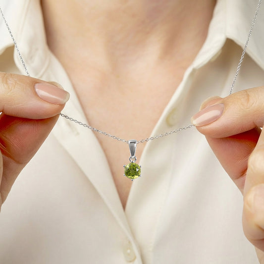 peridot pendant on a silver chain held by hands against a white shirt background