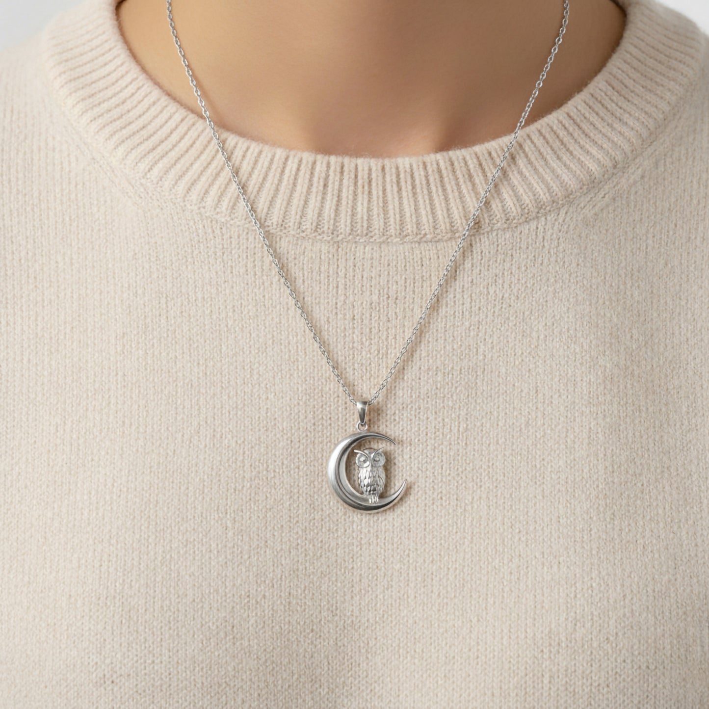 Silver necklace with a crescent moon and owl pendant on a beige sweater.