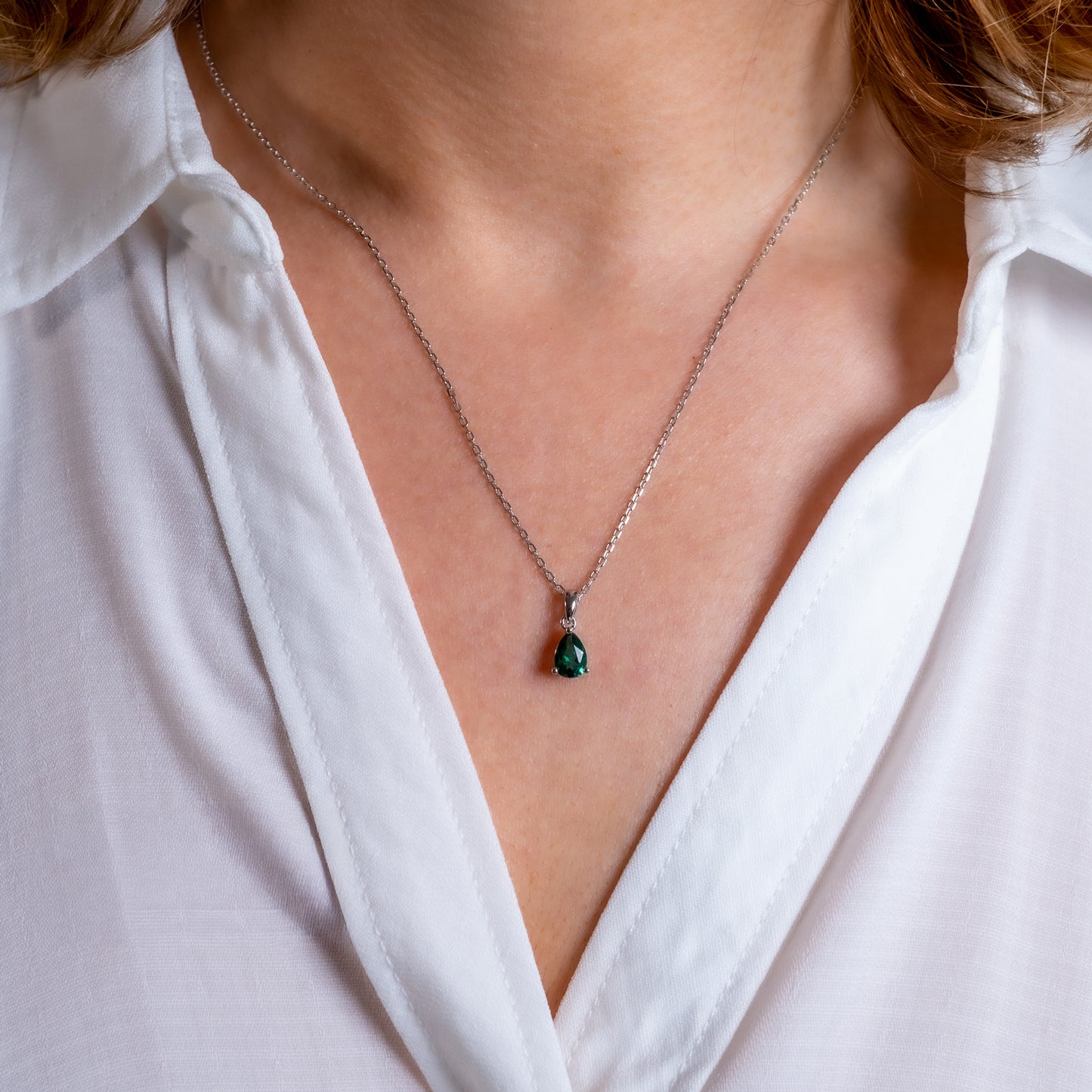Close-up of a necklace with a green pendant worn by a person in a white shirt.