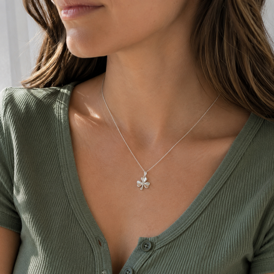 A close-up of a woman wearing a delicate silver shamrock necklace, paired with an olive green ribbed top.