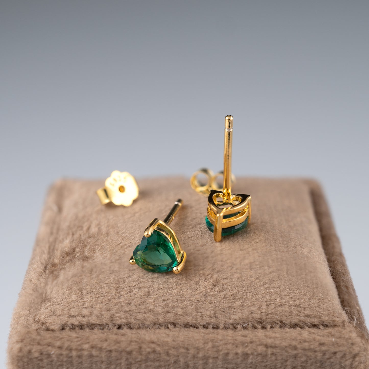 Gold earrings with lab zambian emeralds on a brown jewelry box against a gray background