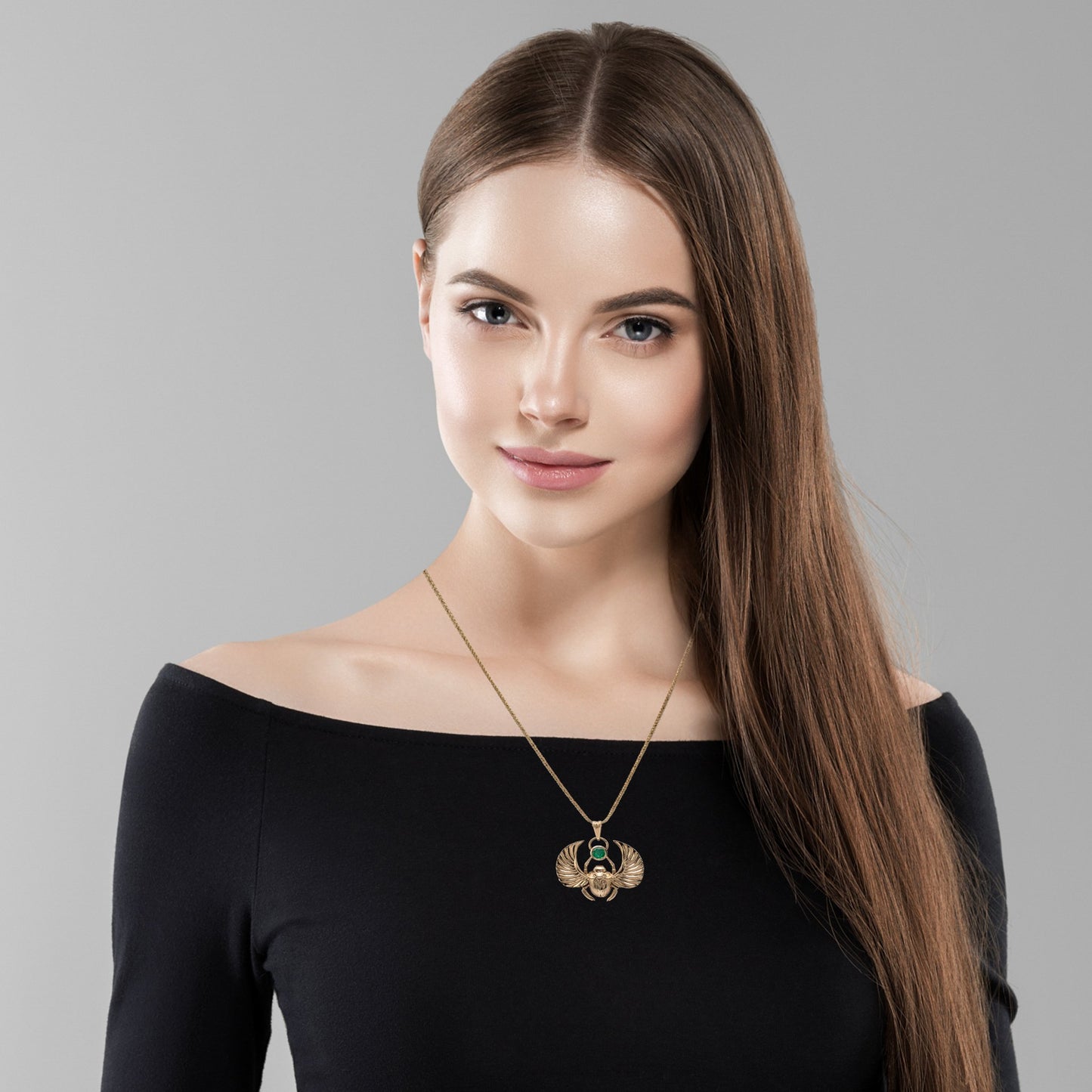 Woman wearing 18K gold winged scarab beetle necklace with emerald