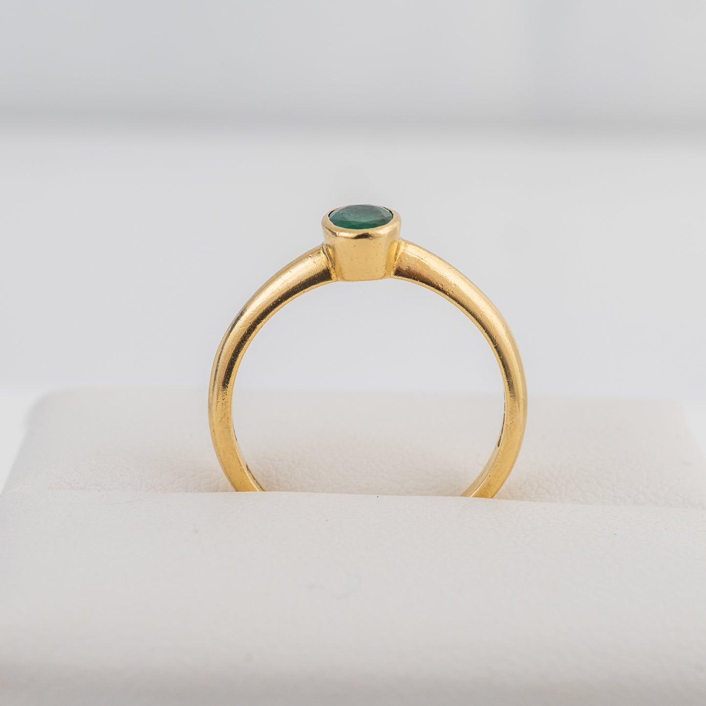 End profile of an 18ct gold emerald solitaire ring with a bezel-set oval emerald