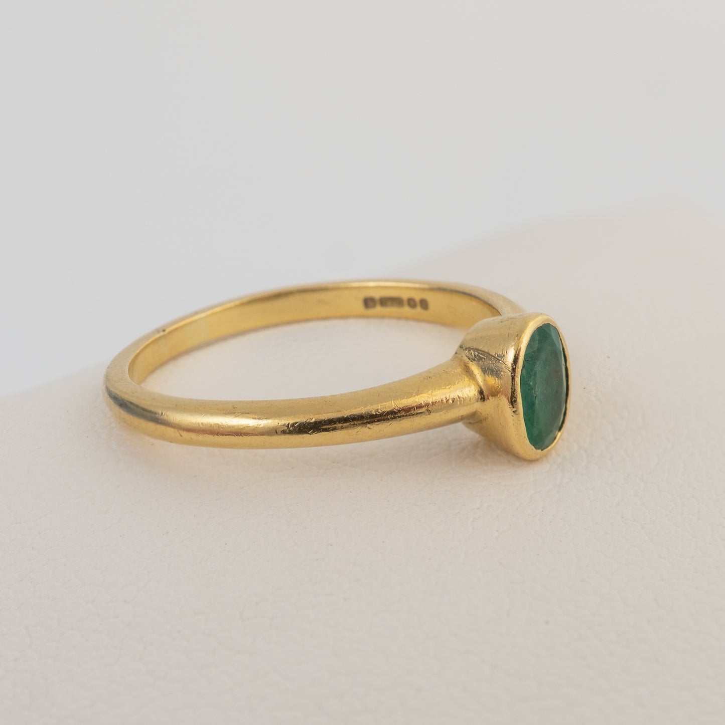 Side profile of an 18ct gold emerald solitaire ring with a bezel-set natural emerald