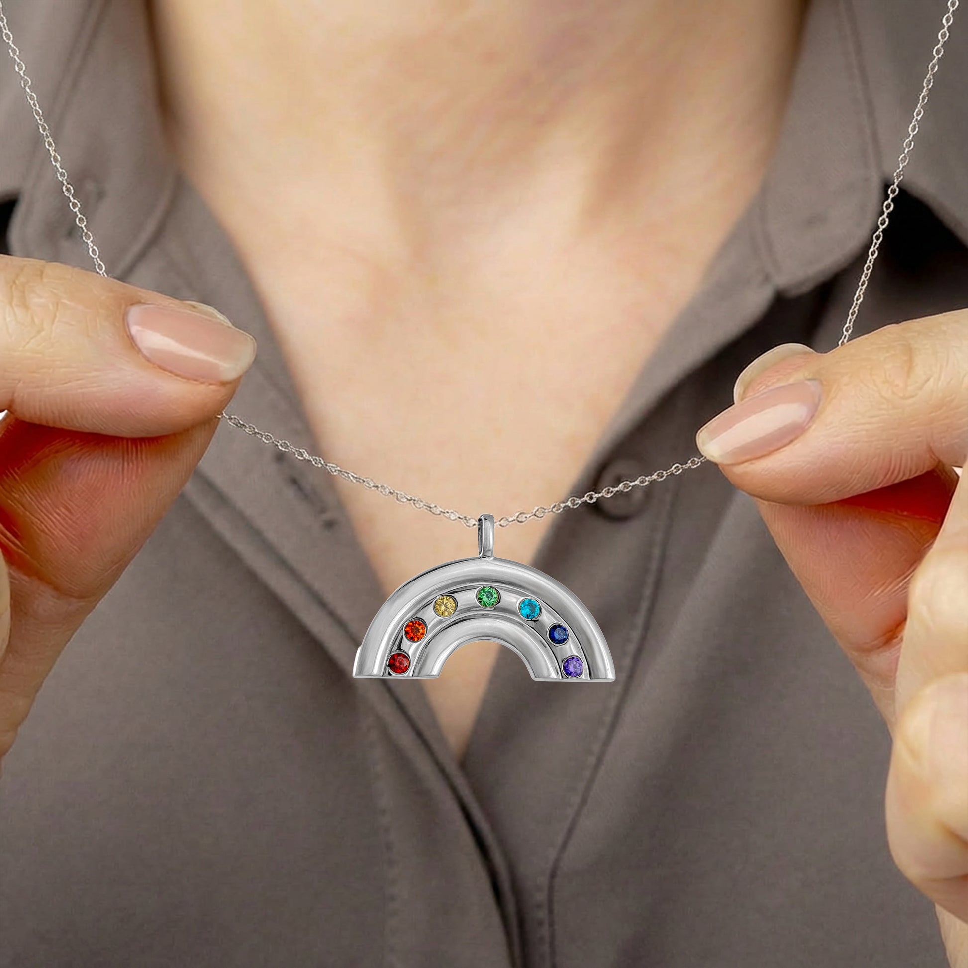 Silver rainbow pendant with colored stones held by a person against a neutral background