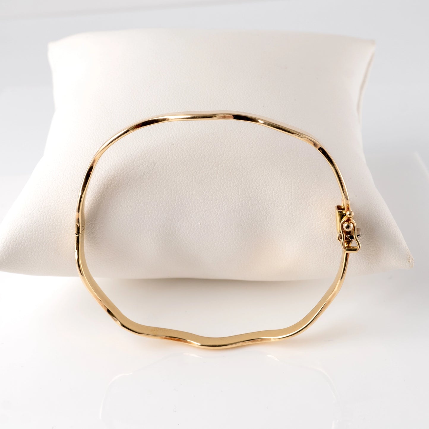 375 gold wave bangle bracelet – side view with hinged clasp on display cushion.