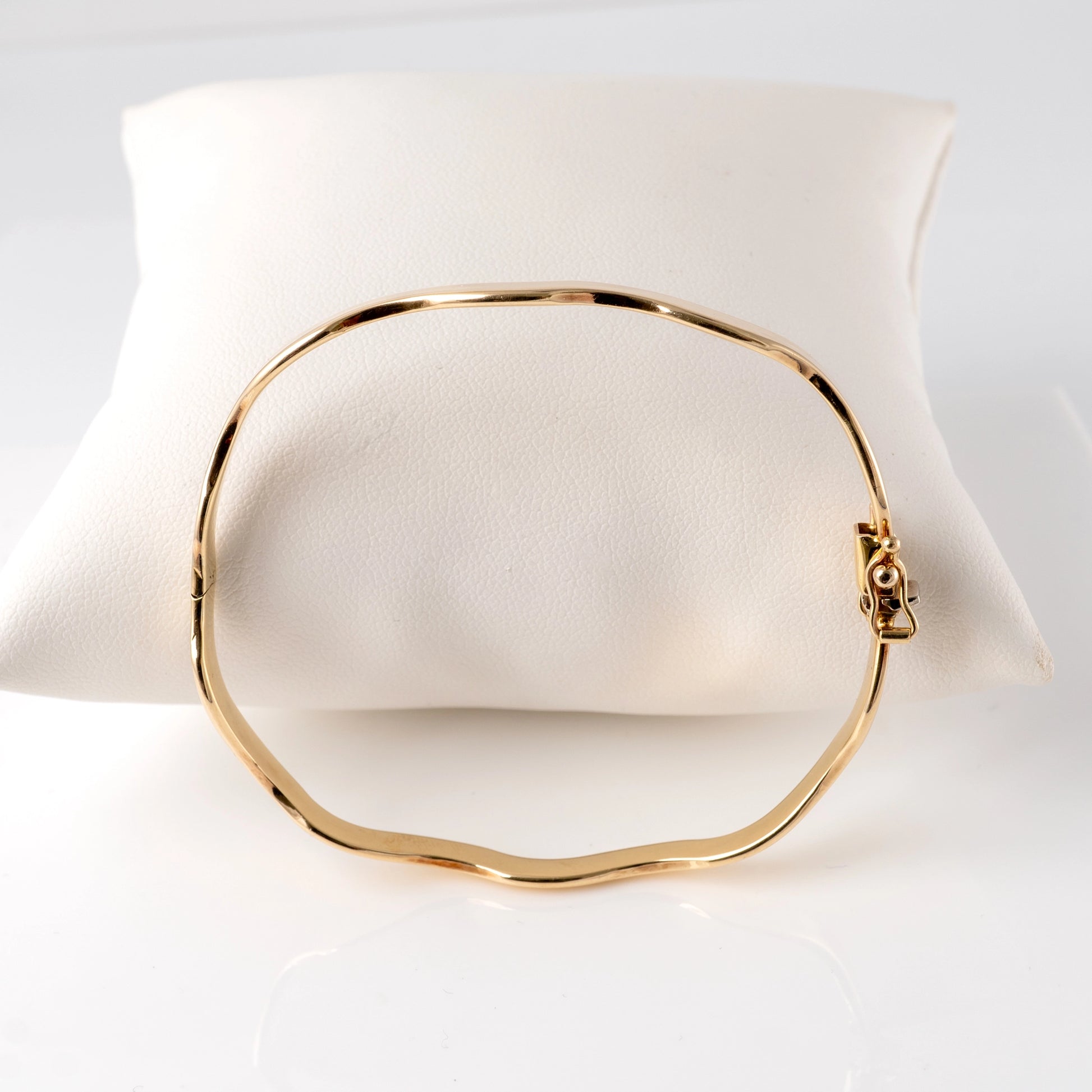 375 gold wave bangle bracelet – side view with hinged clasp on display cushion.