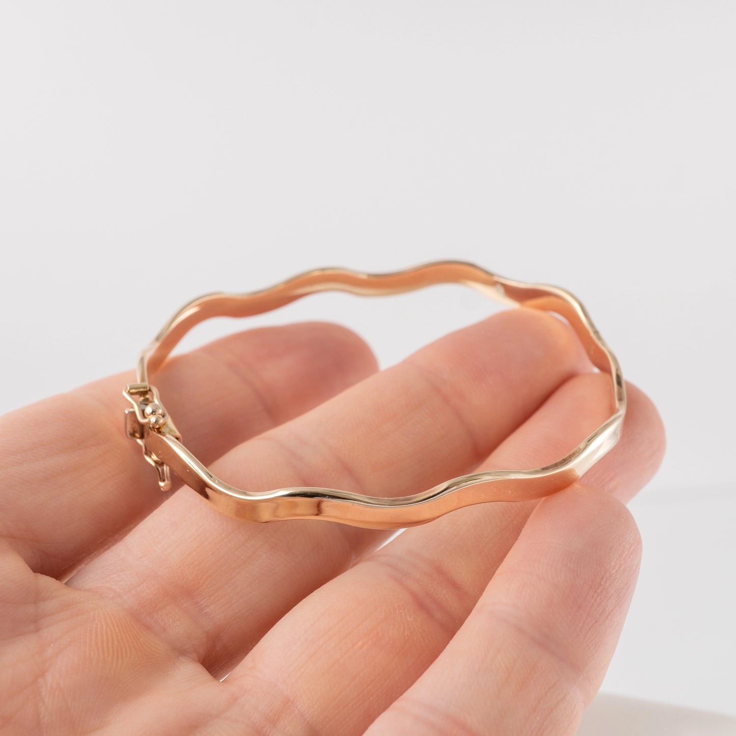 375 gold wave bangle bracelet – held in hand showing scale and clasp detail.