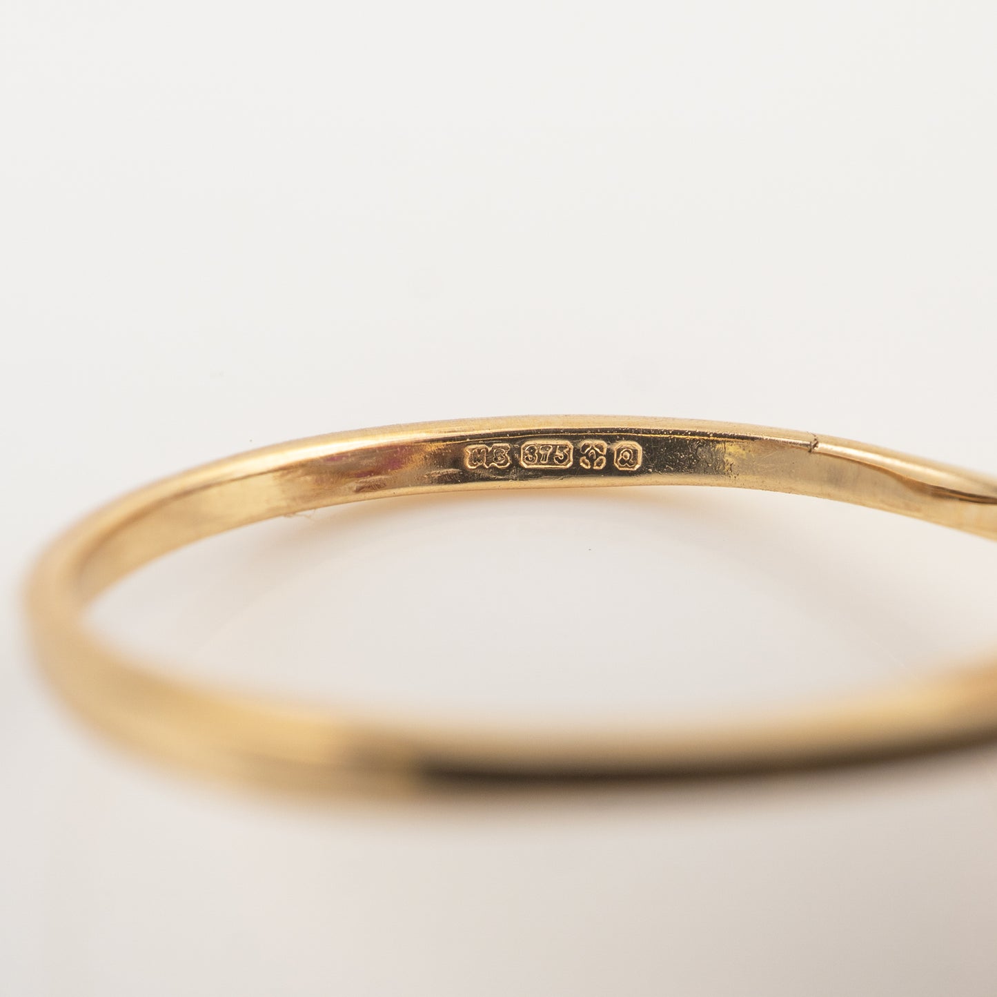 A close-up of a polished yellow gold bangle bracelet, showing a sterling silver purity hallmark stamped on the inside, set against a clean white background.