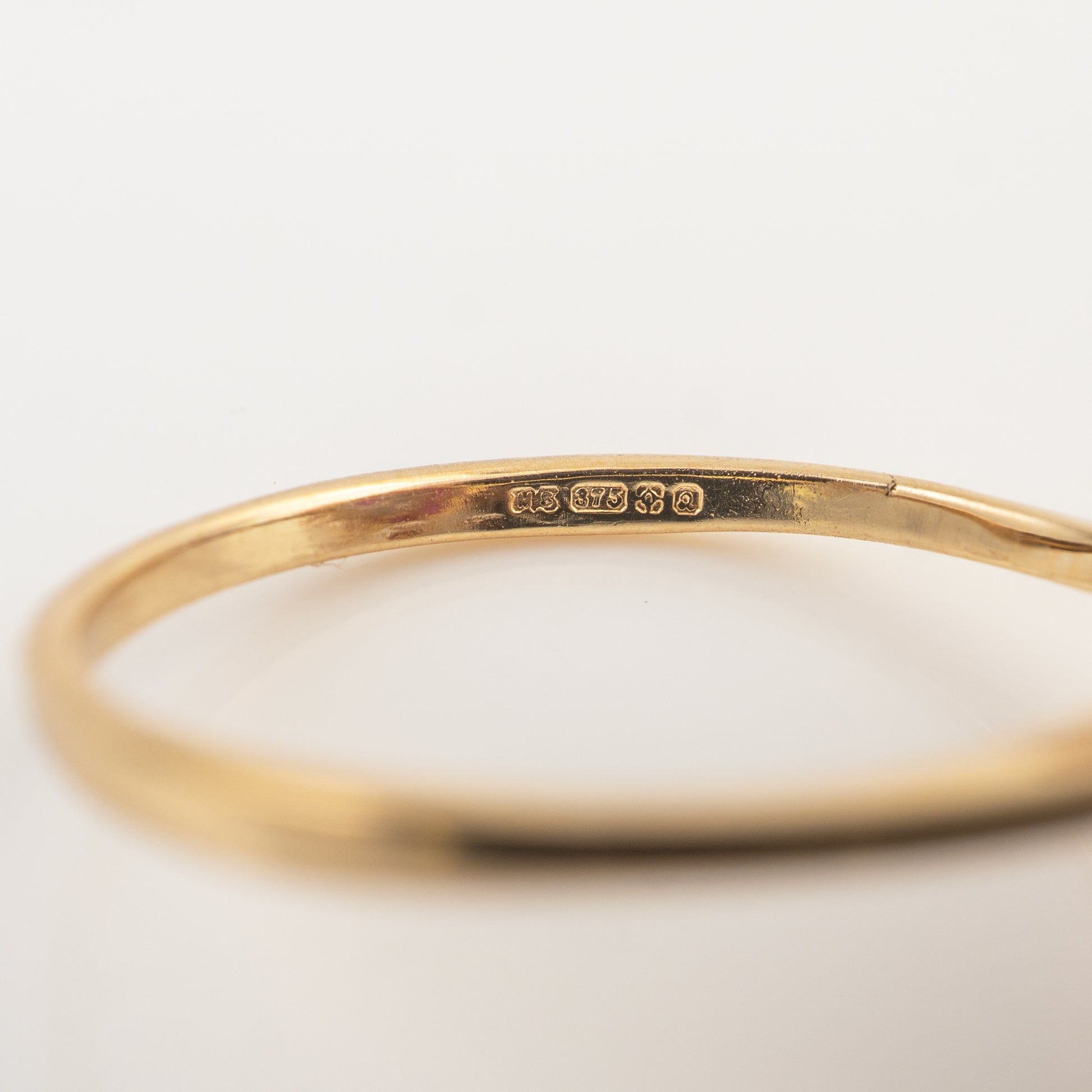 A close-up of a polished yellow gold bangle bracelet, showing a sterling silver purity hallmark stamped on the inside, set against a clean white background.