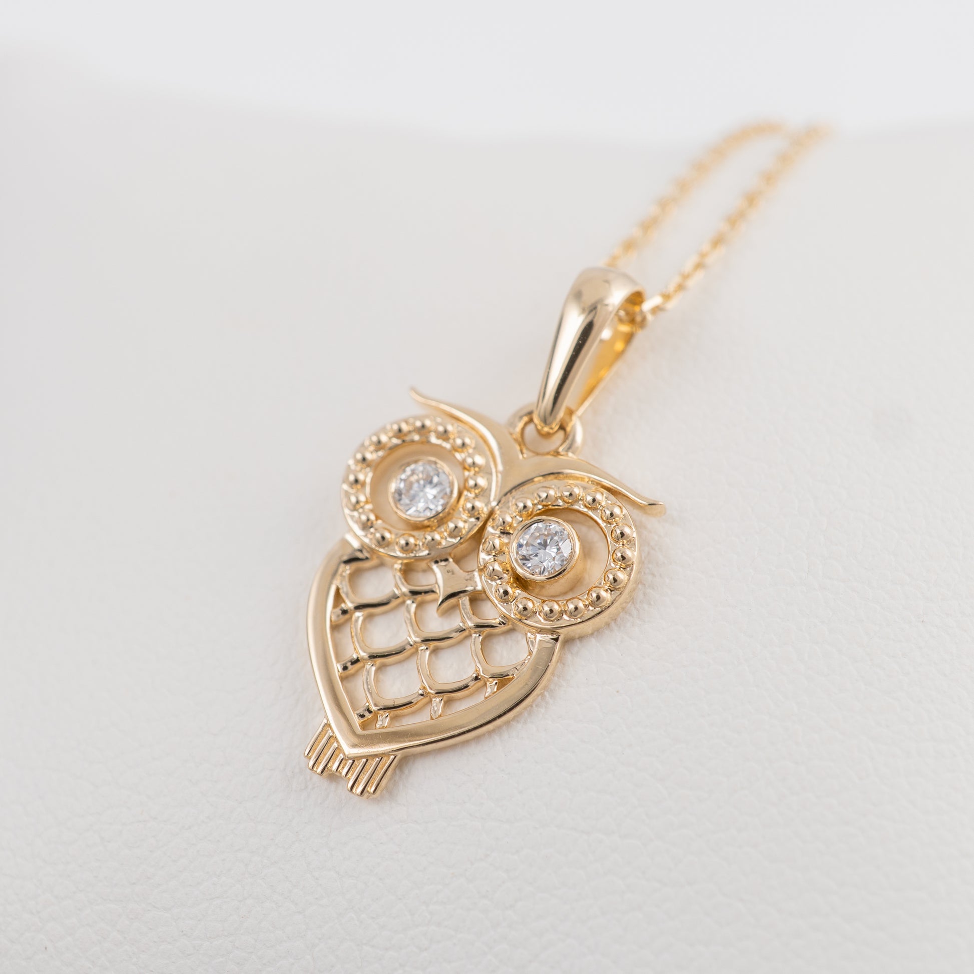 Gold owl-shaped pendant with embedded stones on a light gray background