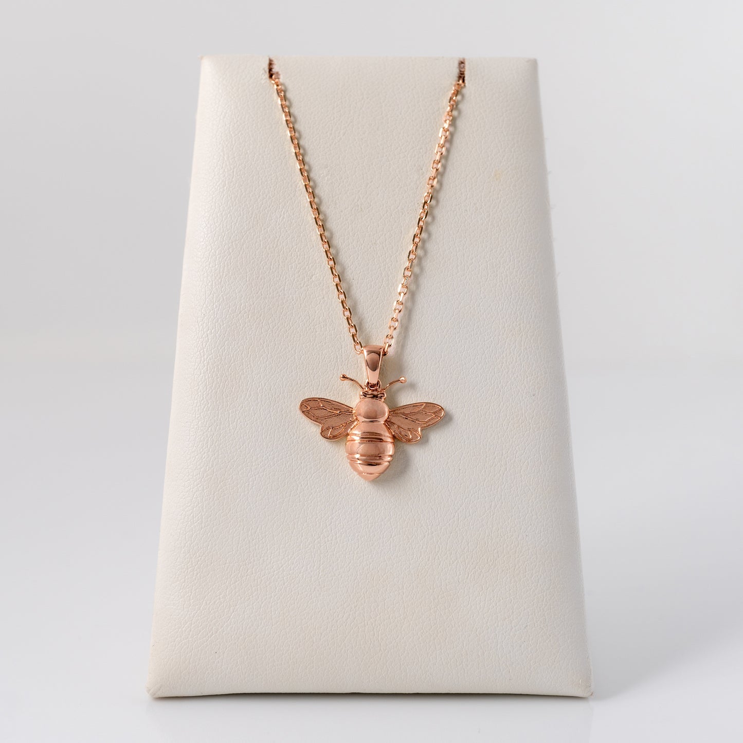 Rose gold bee necklace on a white stand with a light gray background
