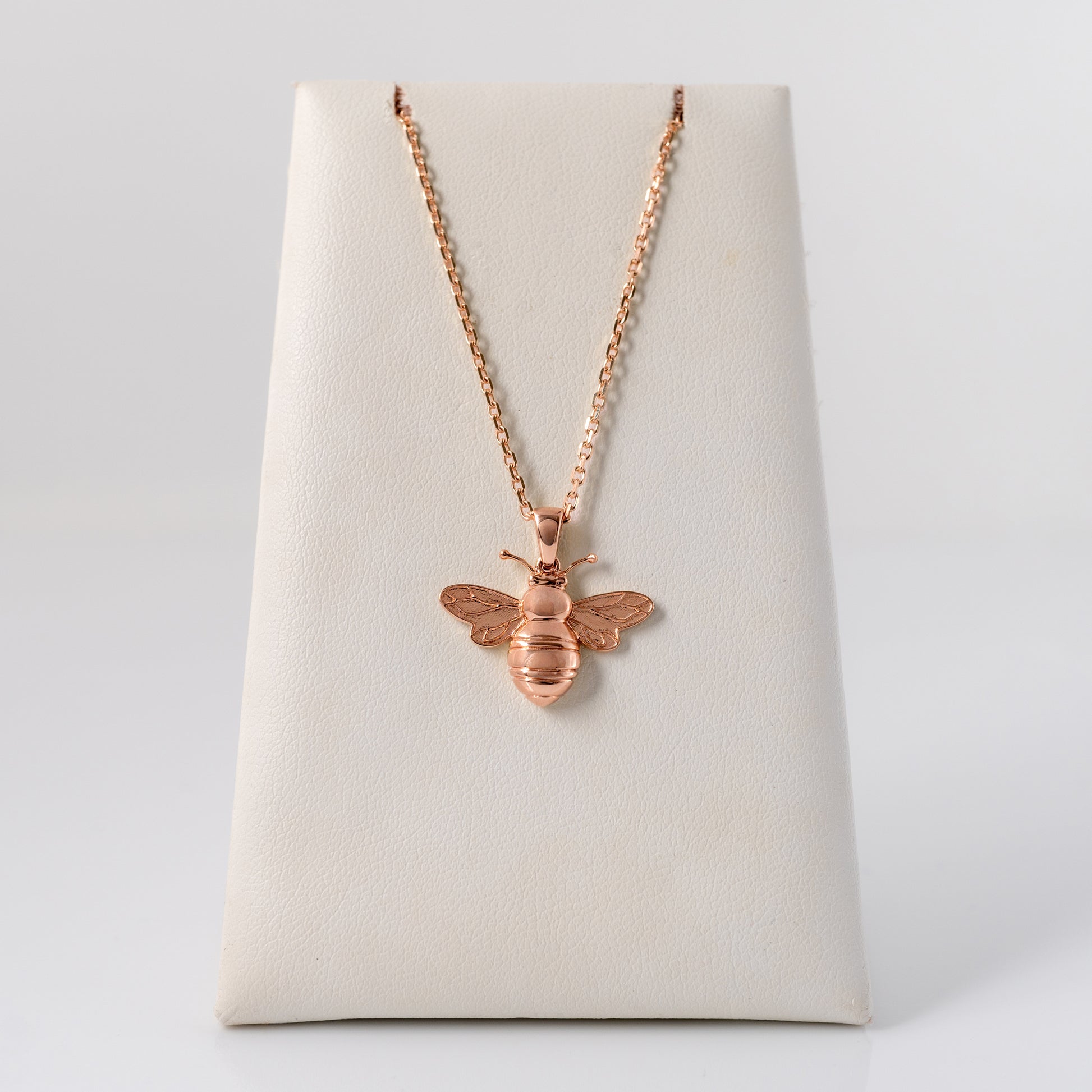 Rose gold bee necklace on a white stand with a light gray background