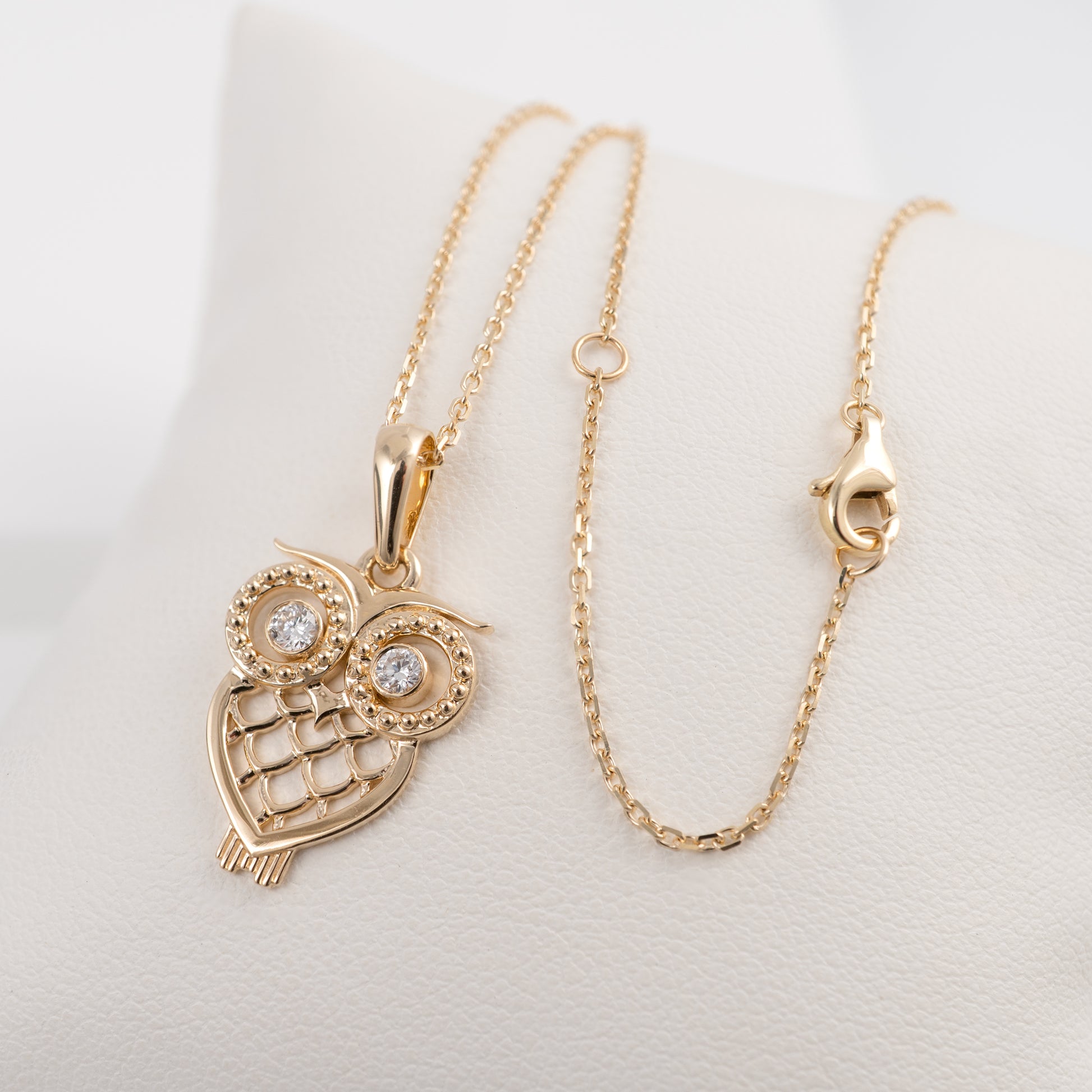 Gold owl-shaped pendant necklace on a light gray background