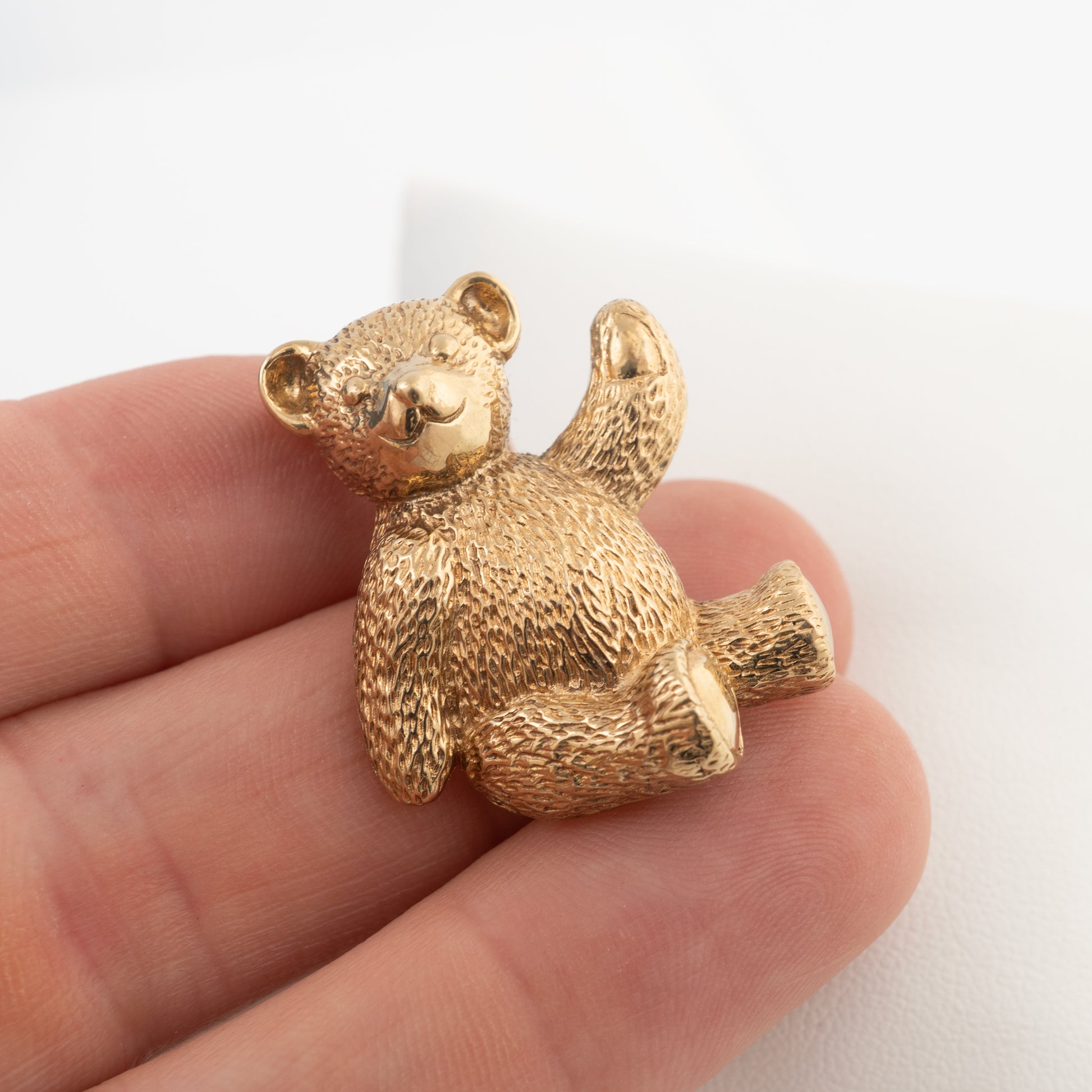 375 gold teddy bear brooch shown on hand to illustrate its size, textured detail and charming design.