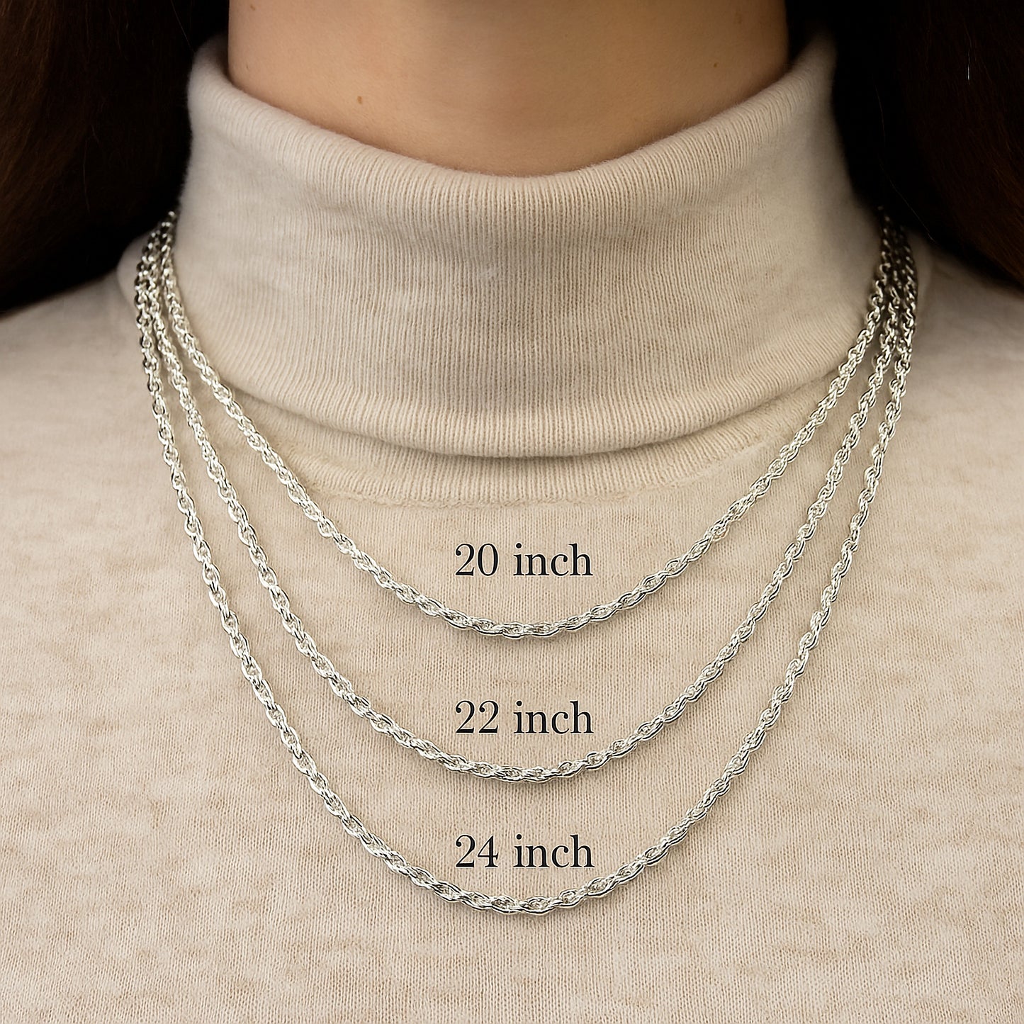 Three silver chains of different lengths worn on a person's neck against a beige background.
