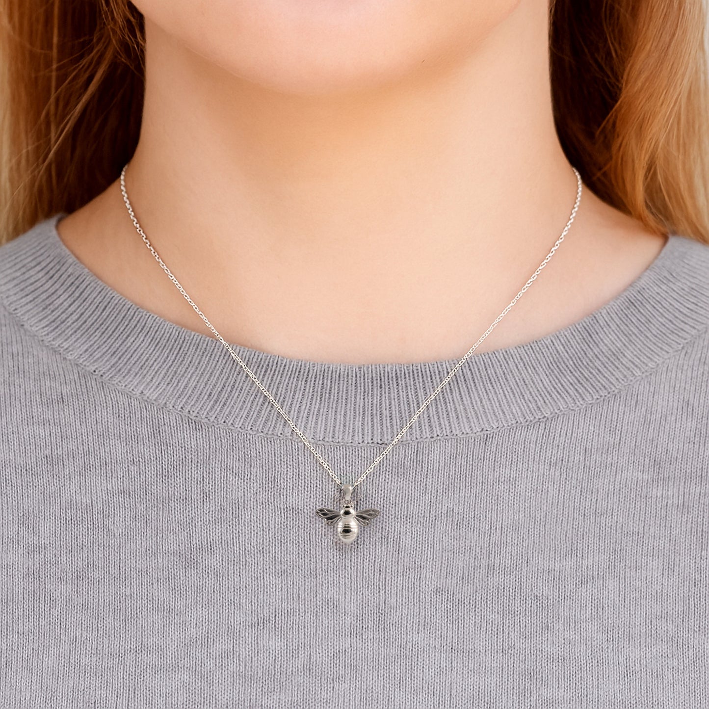Silver bee necklace on a person wearing a gray sweater