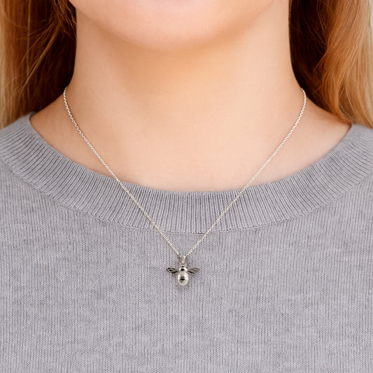 Silver bee necklace on a person wearing a gray sweater