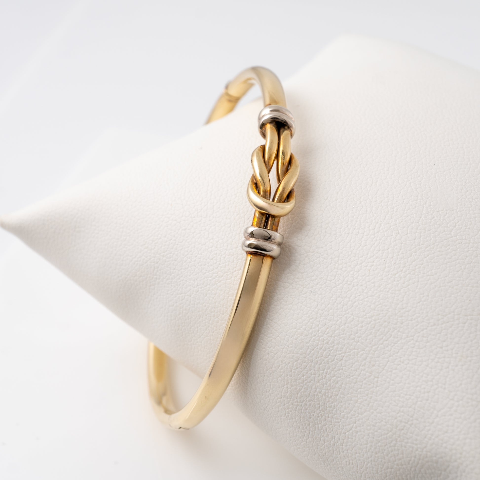 Side view of a 9ct gold lovers knot bangle with white gold accents, displayed on a cushioned surface