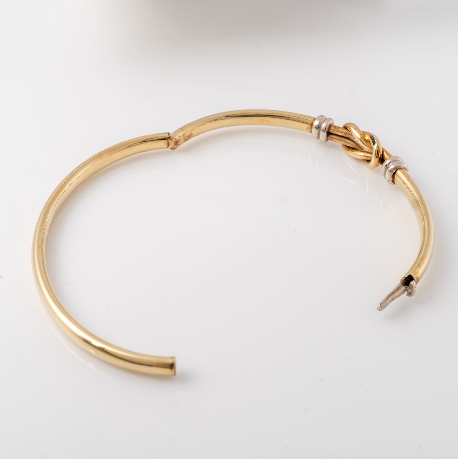 Opened 9ct gold hinge bangle showcasing the trigger catch clasp and white gold knot design detail