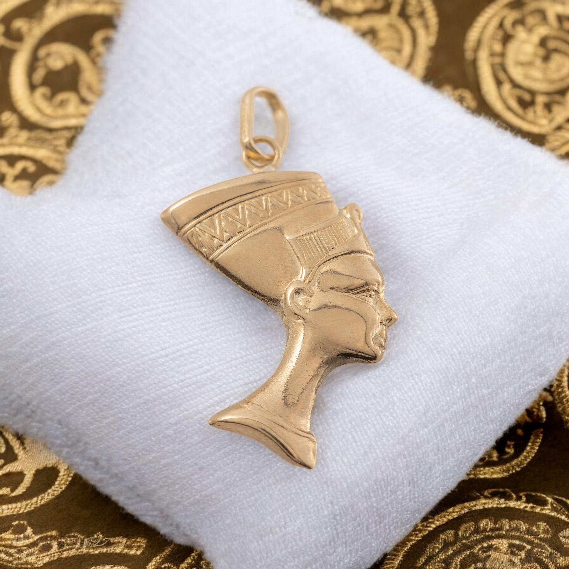 9ct gold Nefertiti pendant displayed on a luxurious white cloth with golden Egyptian patterns