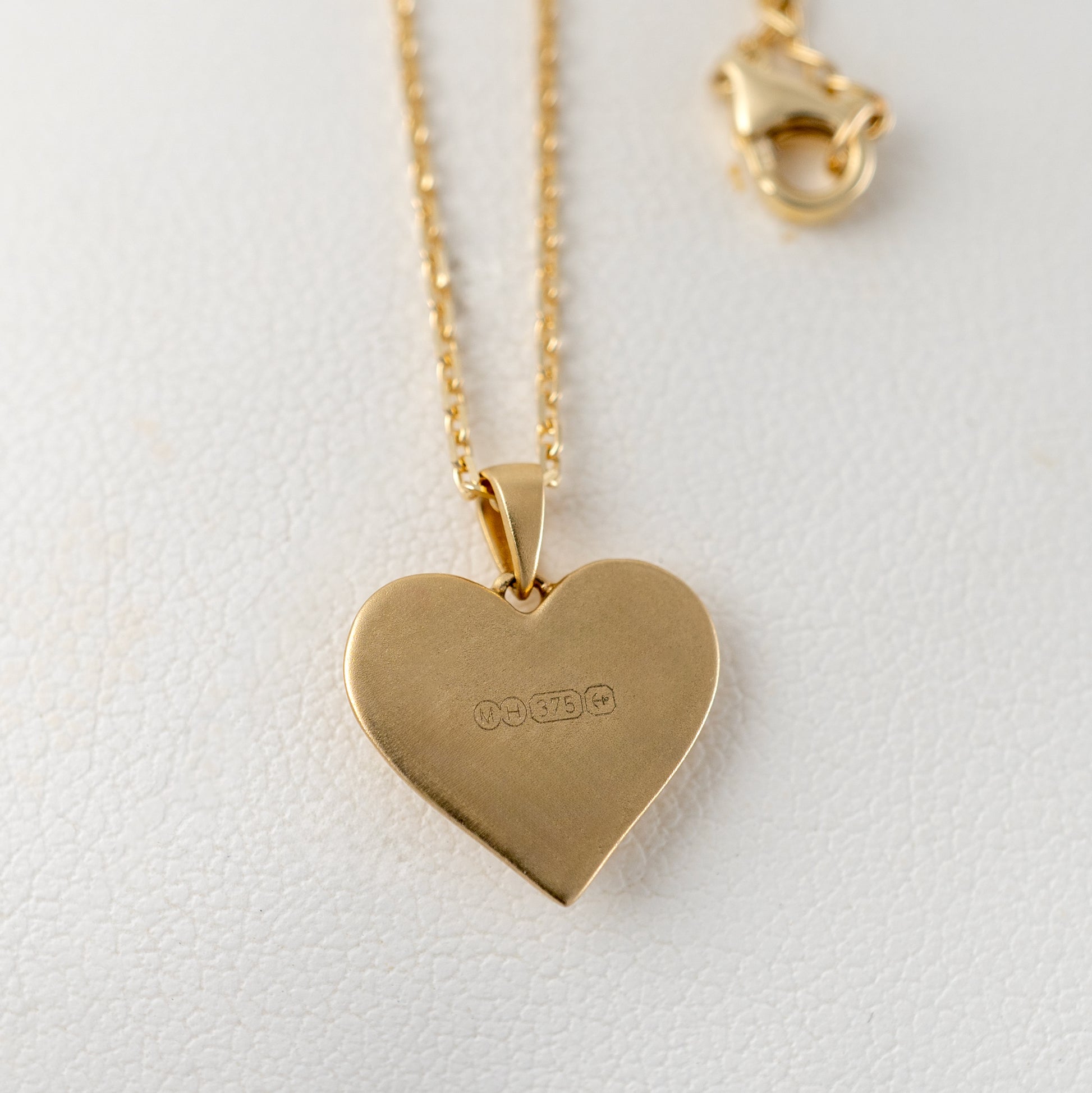 Back view of matte gold heart pendant showing hallmark