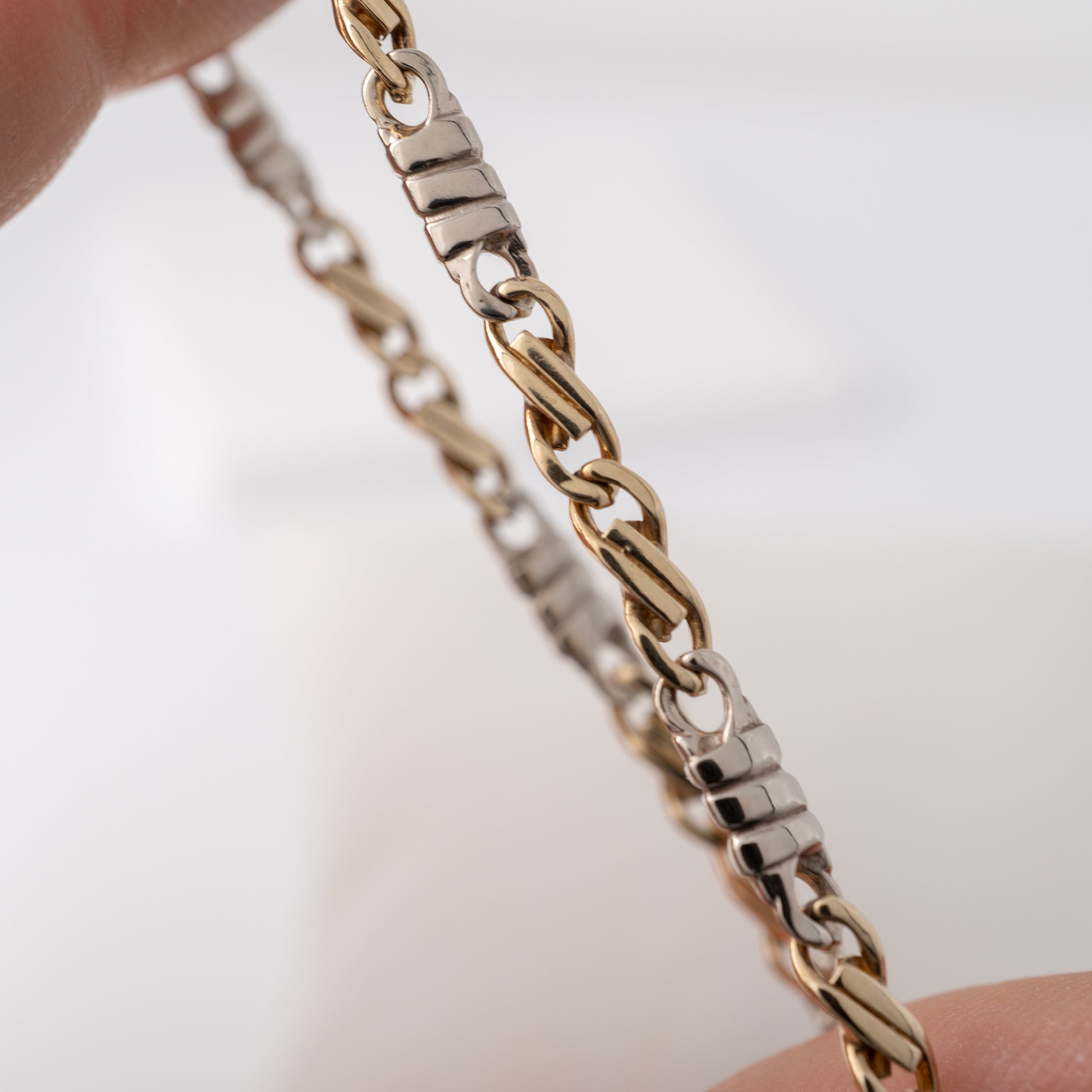 Detail shot of ribbed white gold bar connectors on figaro bracelet gold