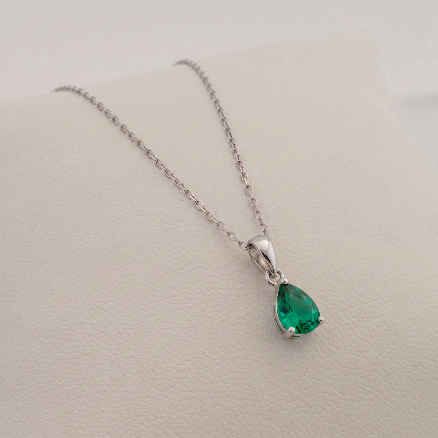 lab emerald necklace pear shape gemstone set in silver side view over a white pad