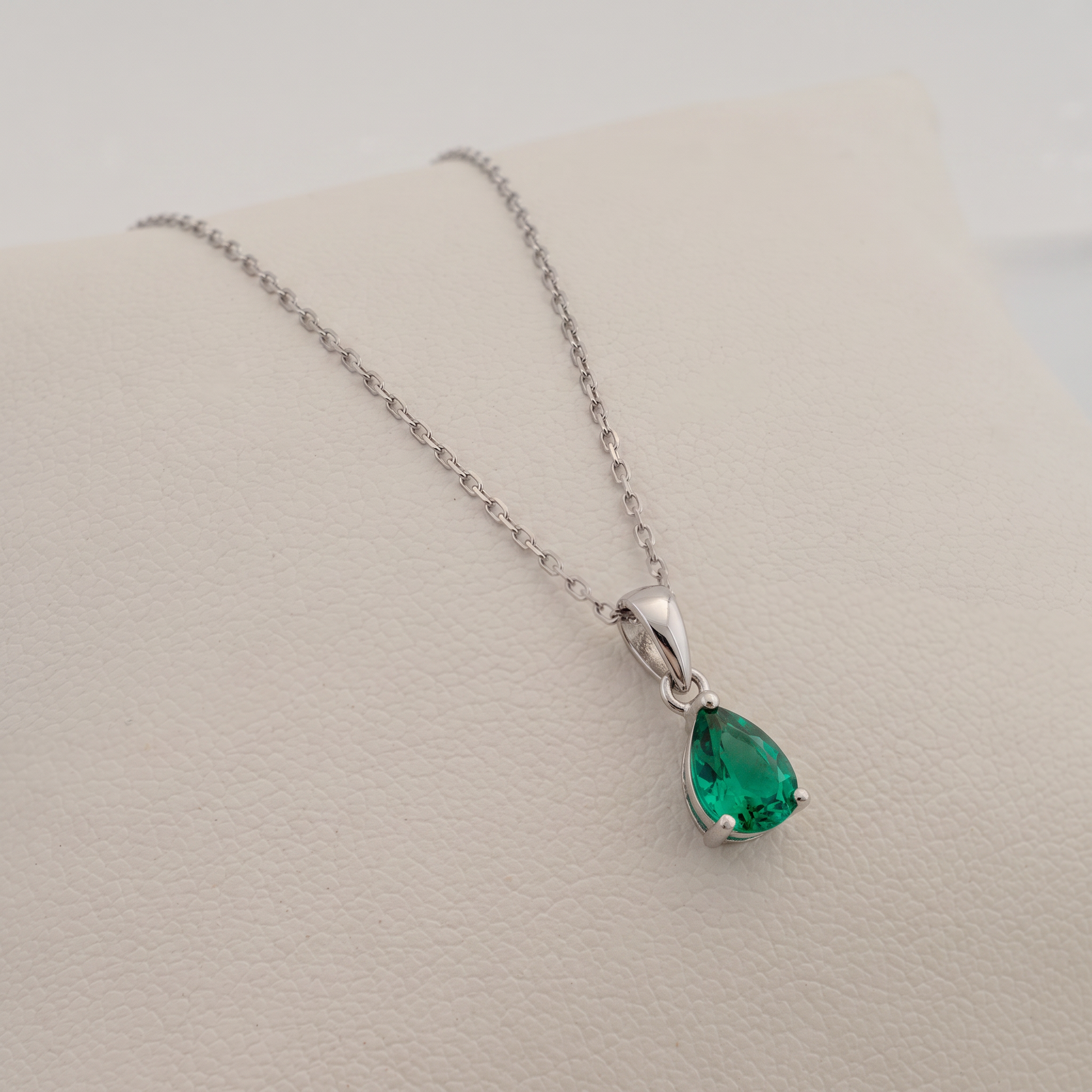lab emerald necklace pear shape gemstone set in silver side view over a white pad