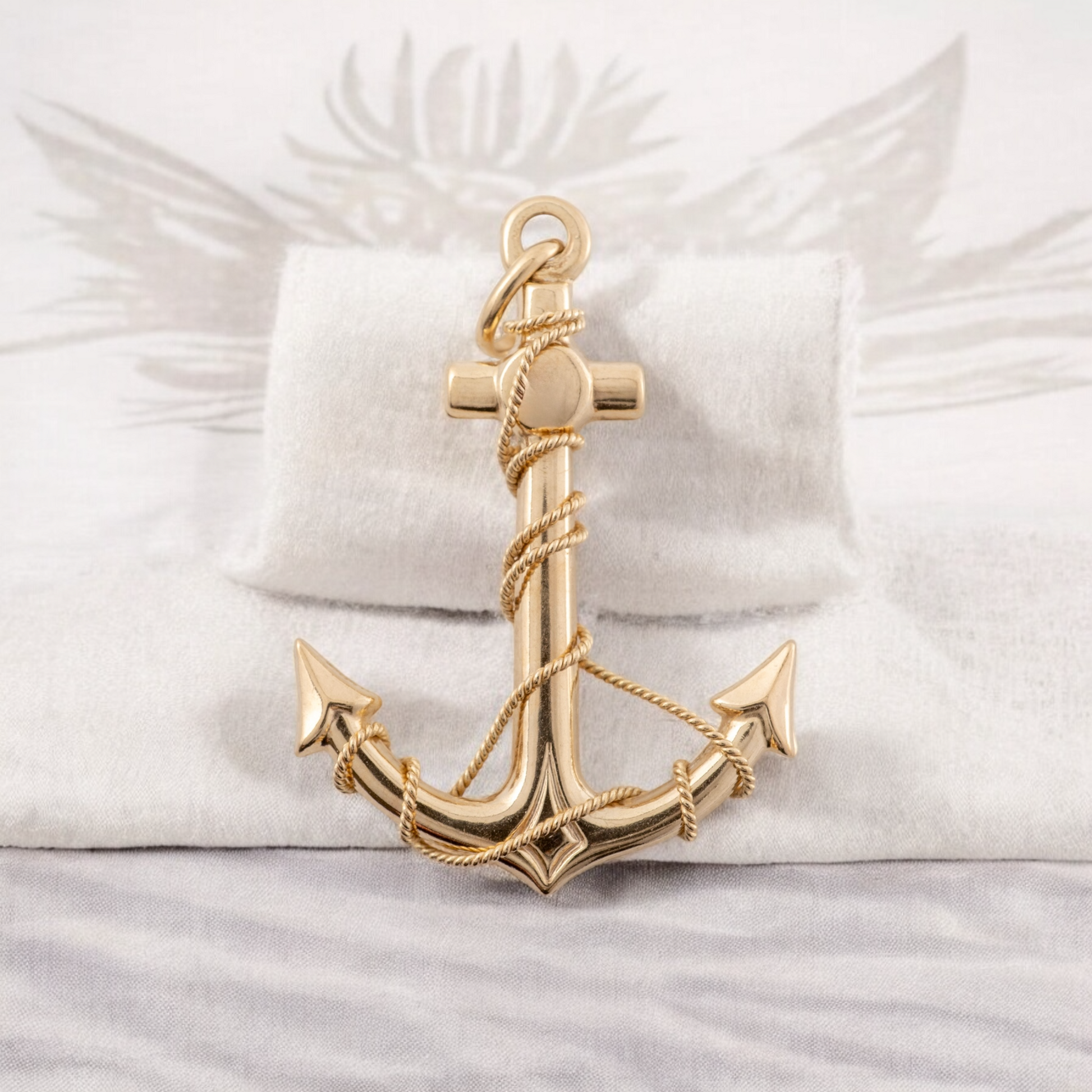 Solid 9ct yellow gold anchor pendant with twisted rope detail, displayed on a soft beige cloth background