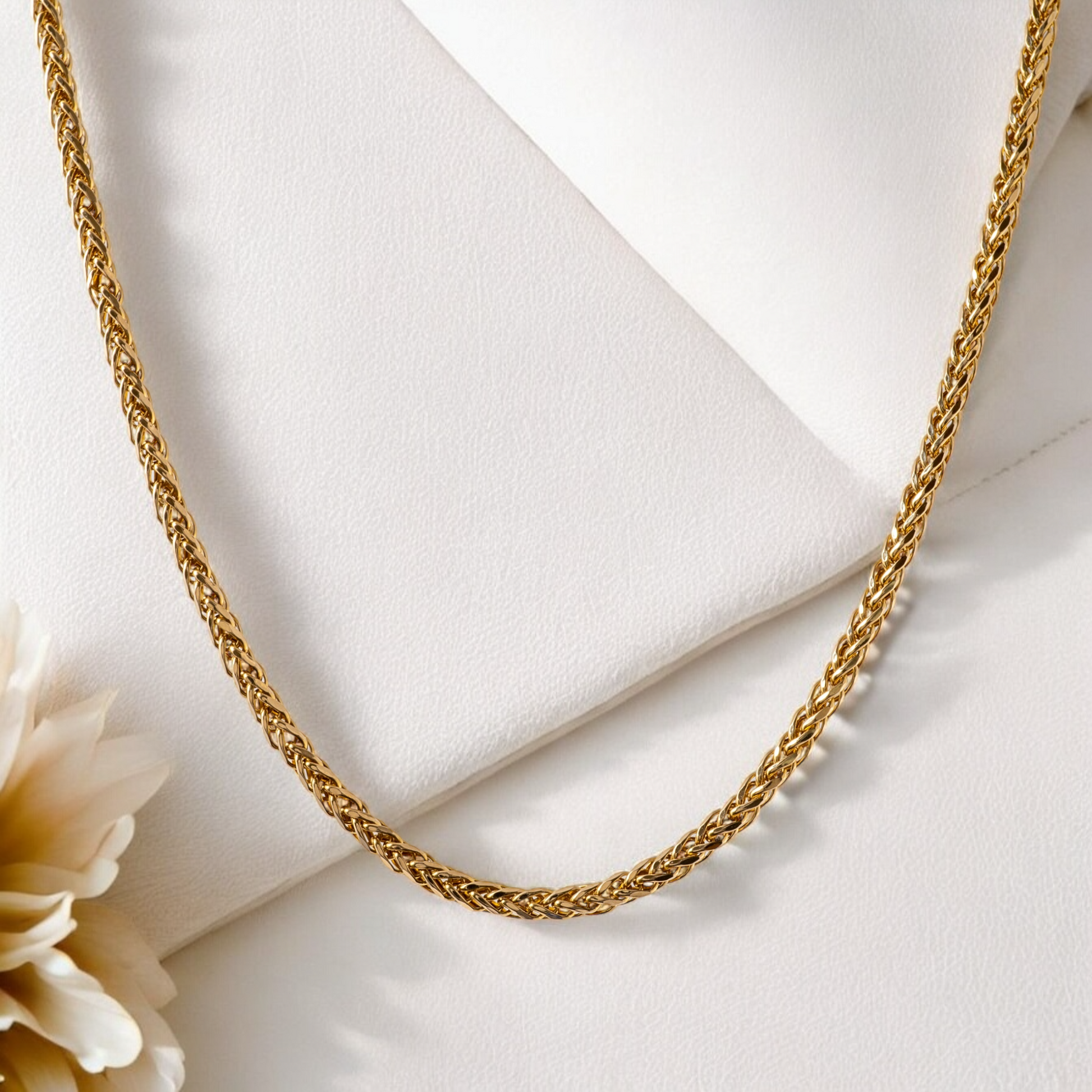 9ct gold spiga chain necklace for women styled on a cream background with a floral accent