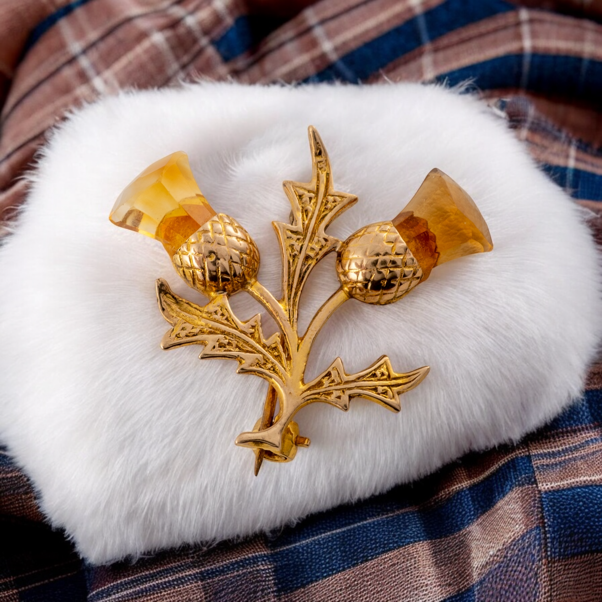 Gold Scottish thistle brooch with citrine gemstones displayed on white fur with a tartan background