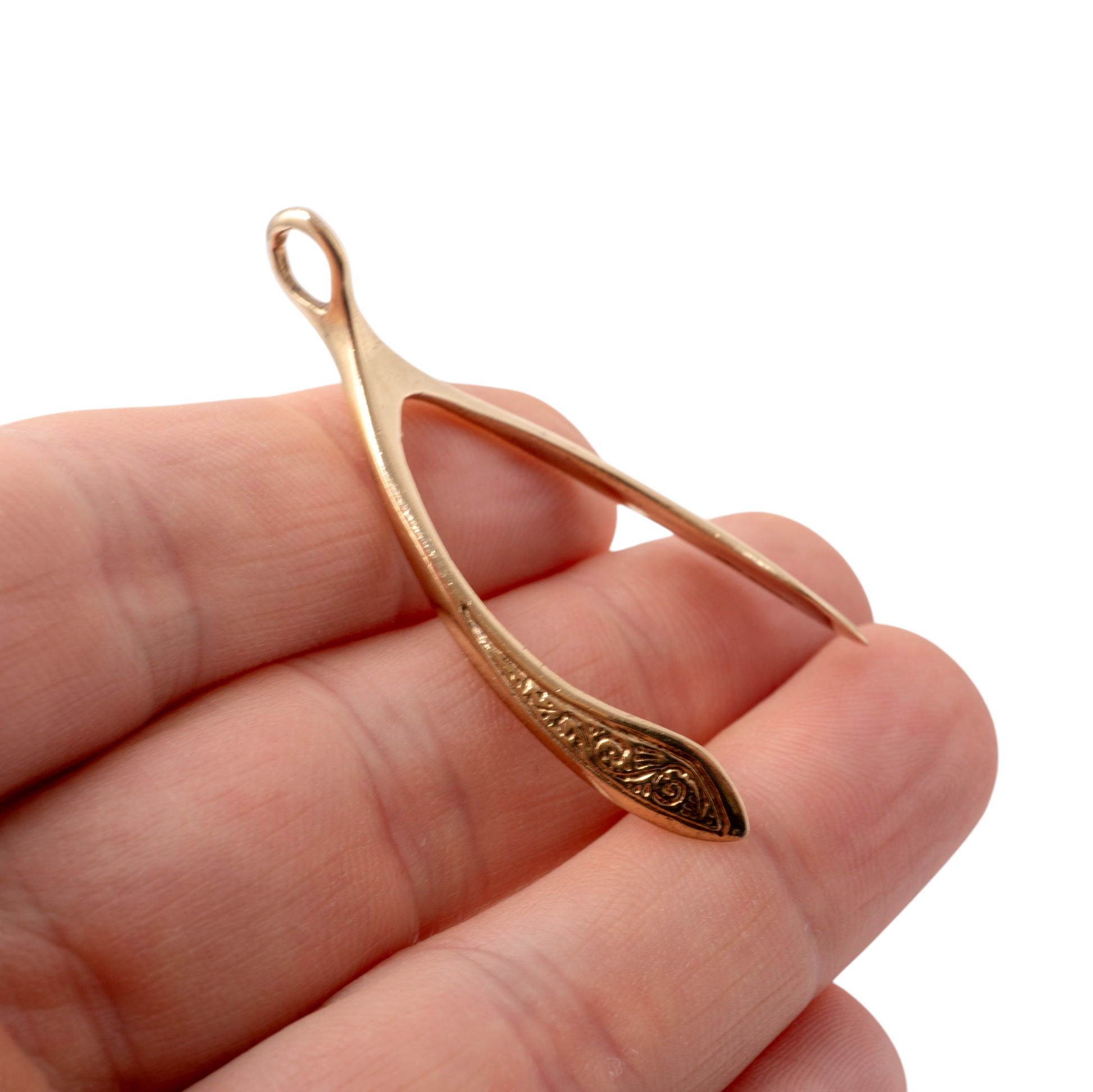Large gold wishbone pendant held in hand, highlighting its intricate scroll detailing and scale.