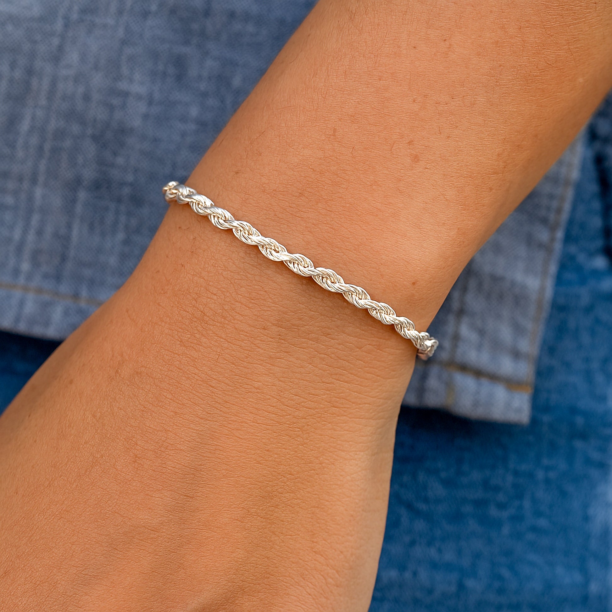 Silver braided bracelet on a wrist with a blue background