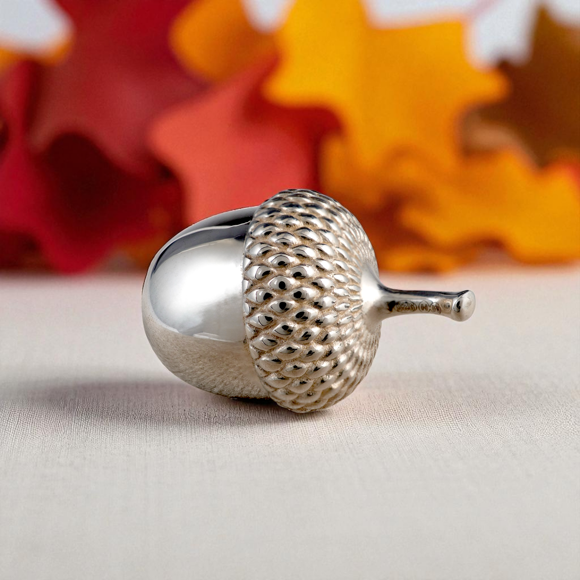 Hallmarked sterling silver acorn ornament with autumn leaves background – symbolic gift and collectable