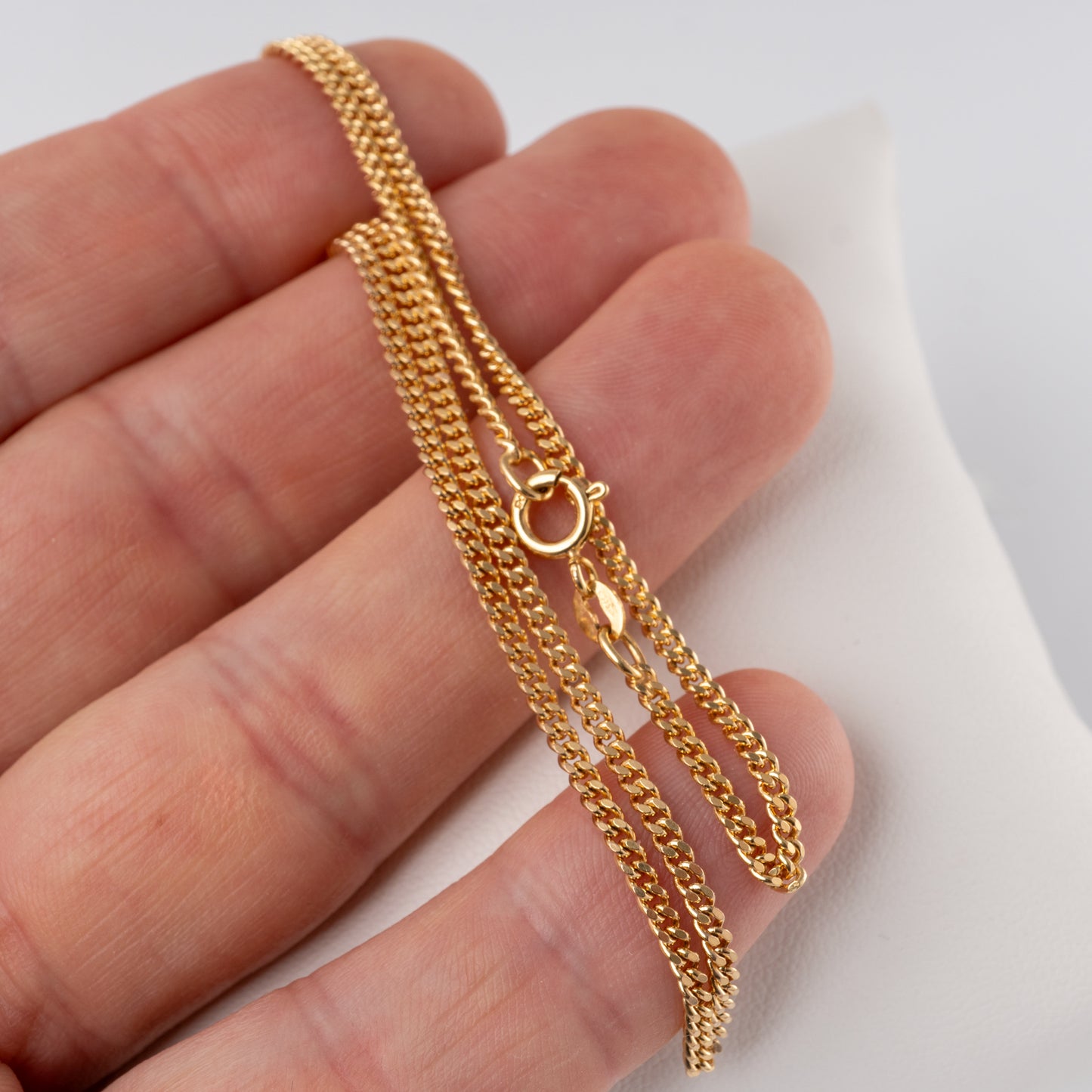 9ct gold flat curb link chain necklace held in hand, showing spring ring clasp and hallmark tag