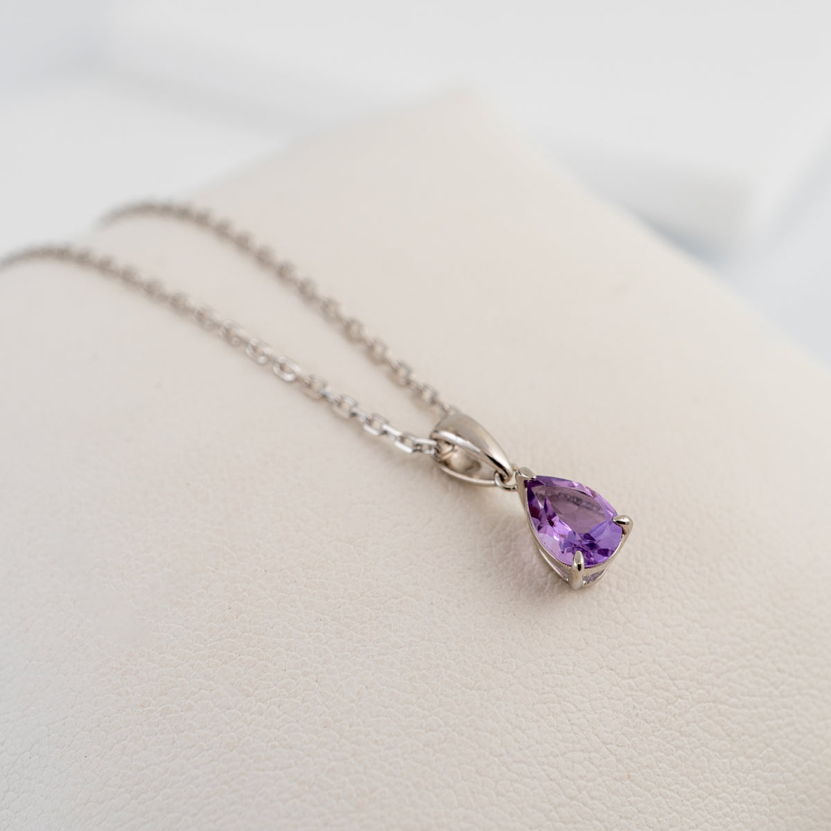 Sterling silver amethyst teardrop pendant resting on a cream-coloured jewellery display stand.