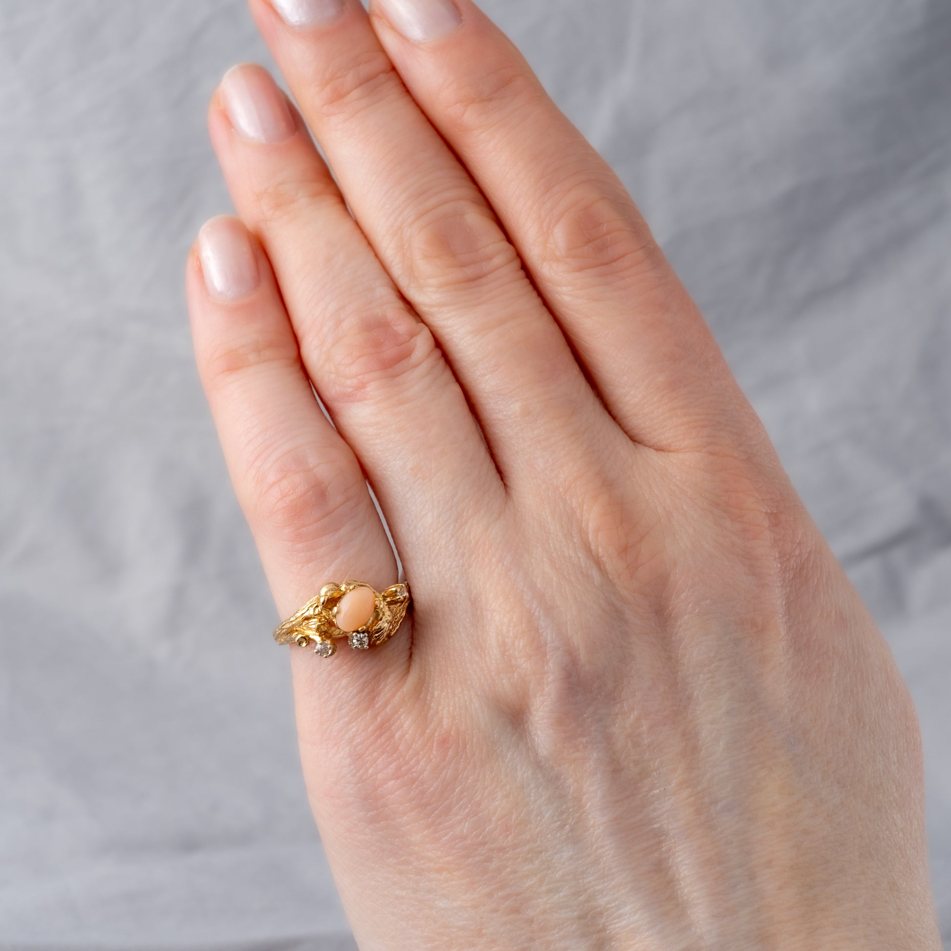 Vintage coral ring on woman’s hand to showcase size and fit, designed in a tree bark gold setting