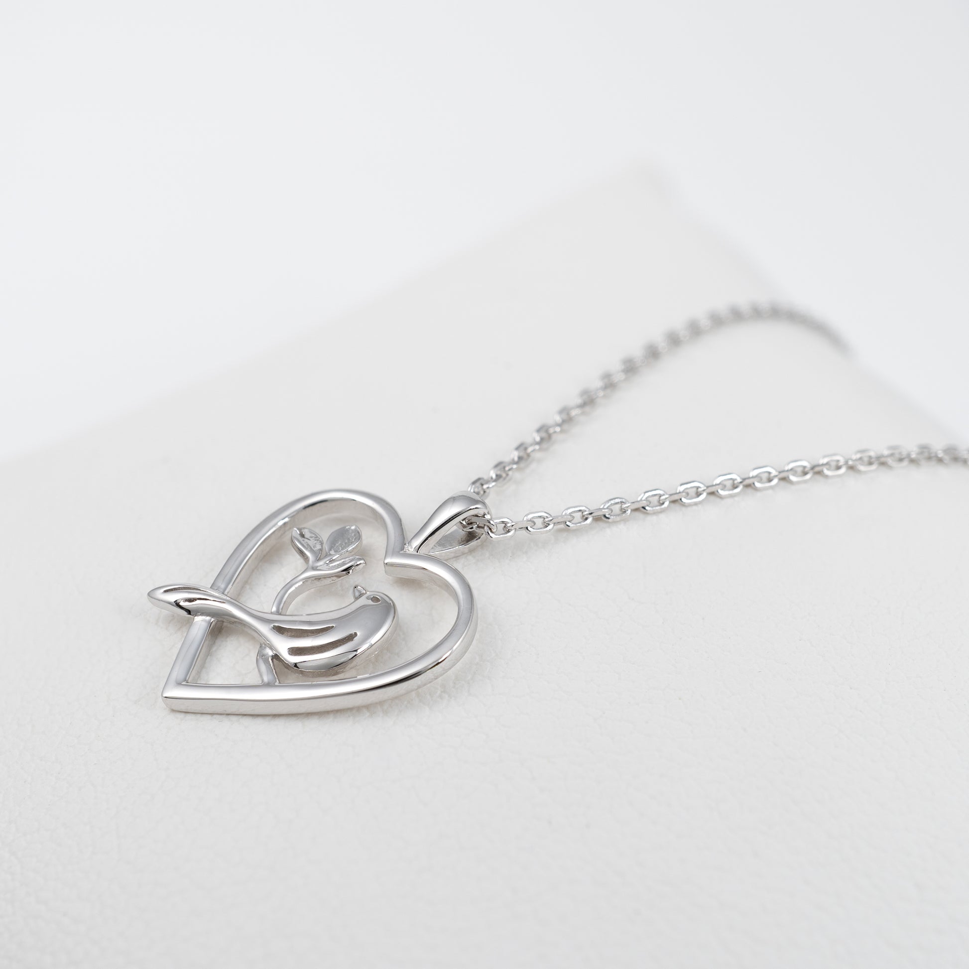 Sterling silver bird heart necklace laid flat at an angle