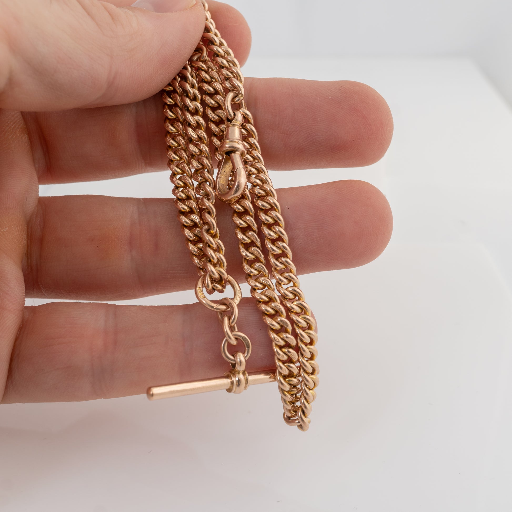 Antique 9ct rose gold Double Albert watch chain held in hand showing original T-bar, dog clip and hallmarked curb links