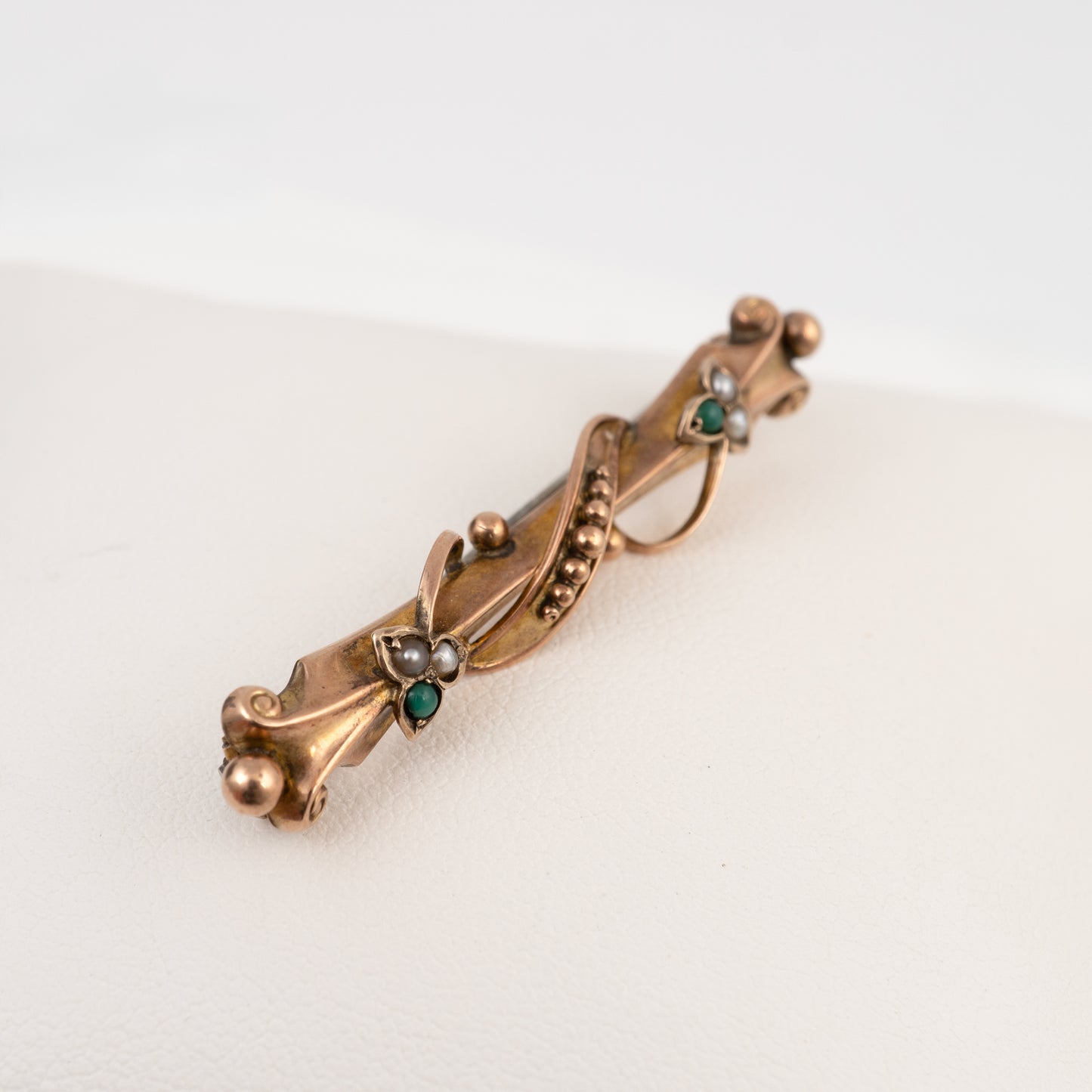 An antique Victorian-style gold-toned brooch featuring a twisted vine design with small green and white gemstones, displayed on a clean white surface.