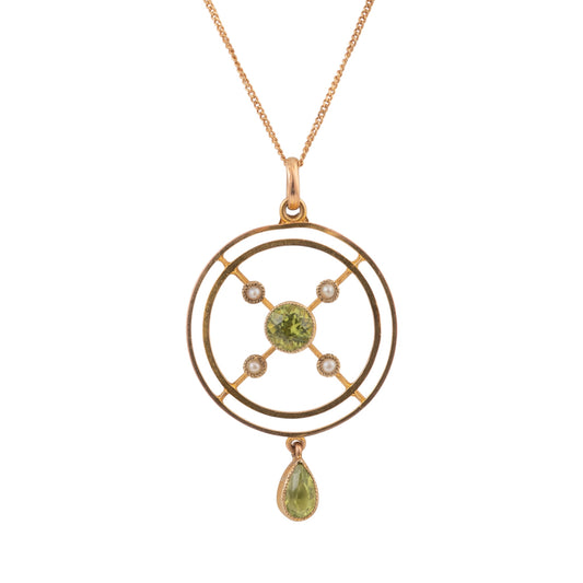 A gold pendant necklace featuring a circular geometric design with a central green peridot gemstone, small clear accent stones, and a dangling teardrop-shaped green gemstone, shown on a plain white background.