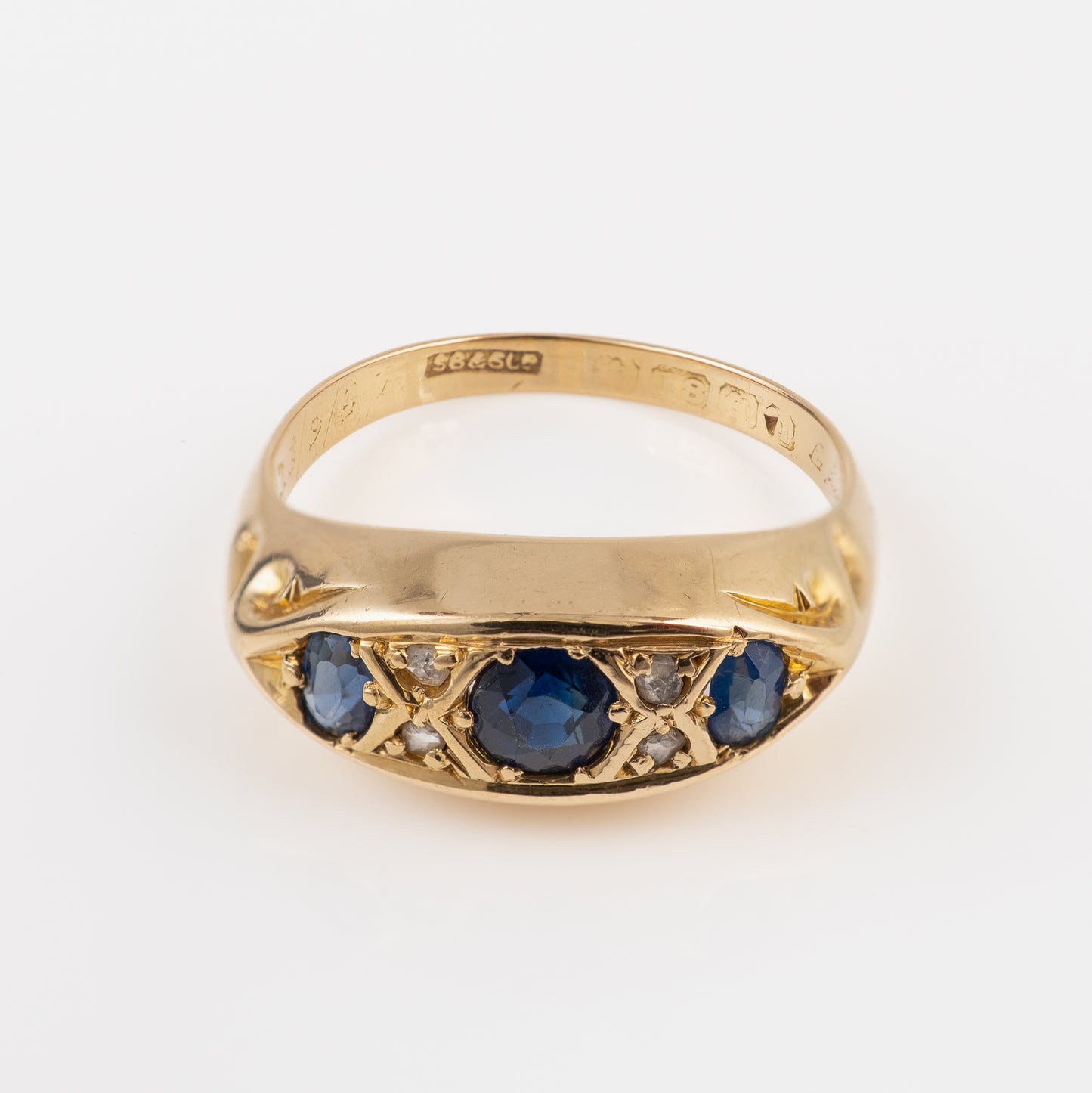 Antique yellow gold signet ring featuring a central round blue sapphire flanked by smaller blue sapphires and small clear stones, set against a plain white background.