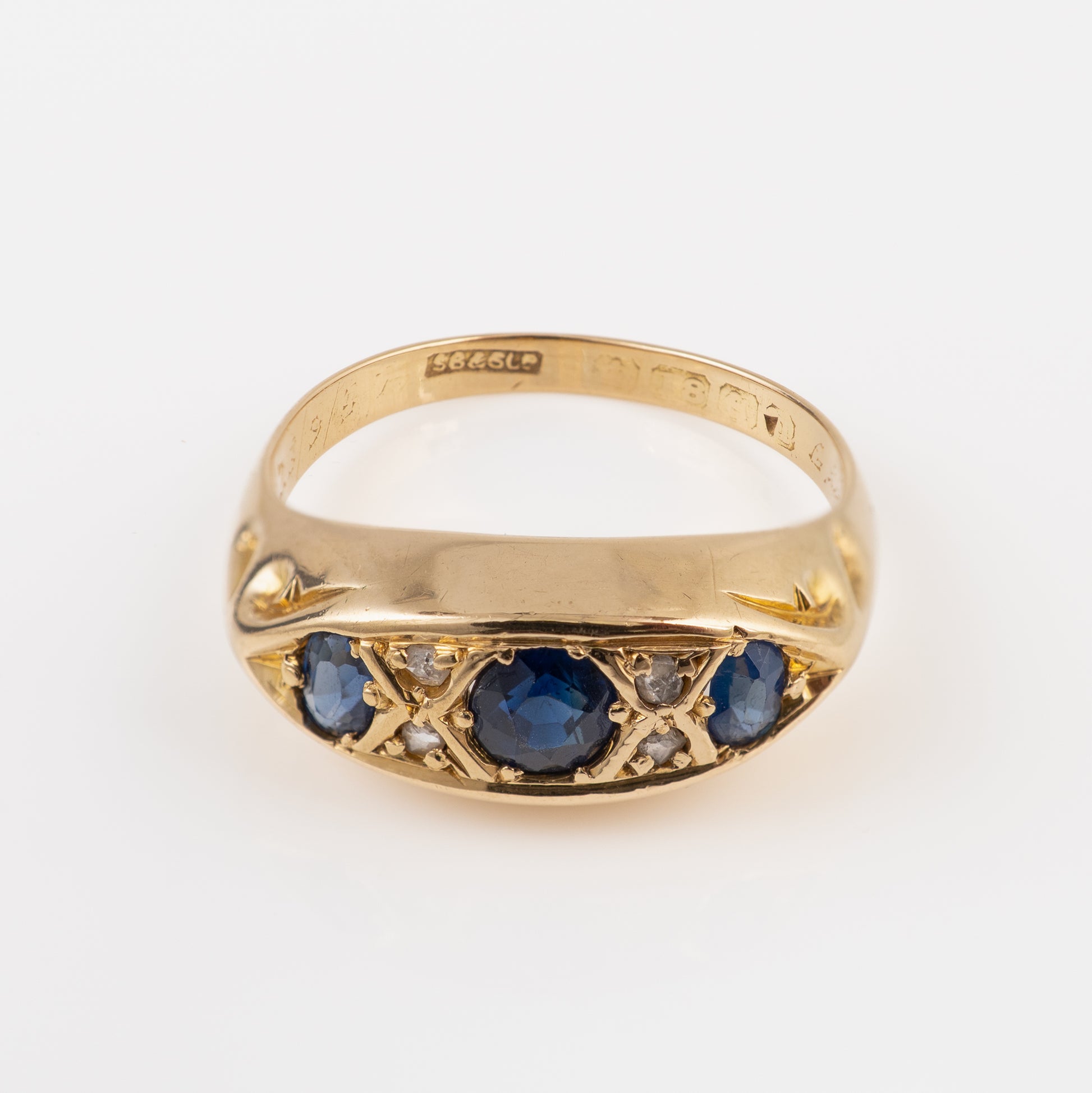 Antique yellow gold signet ring featuring a central round blue sapphire flanked by smaller blue sapphires and small clear stones, set against a plain white background.